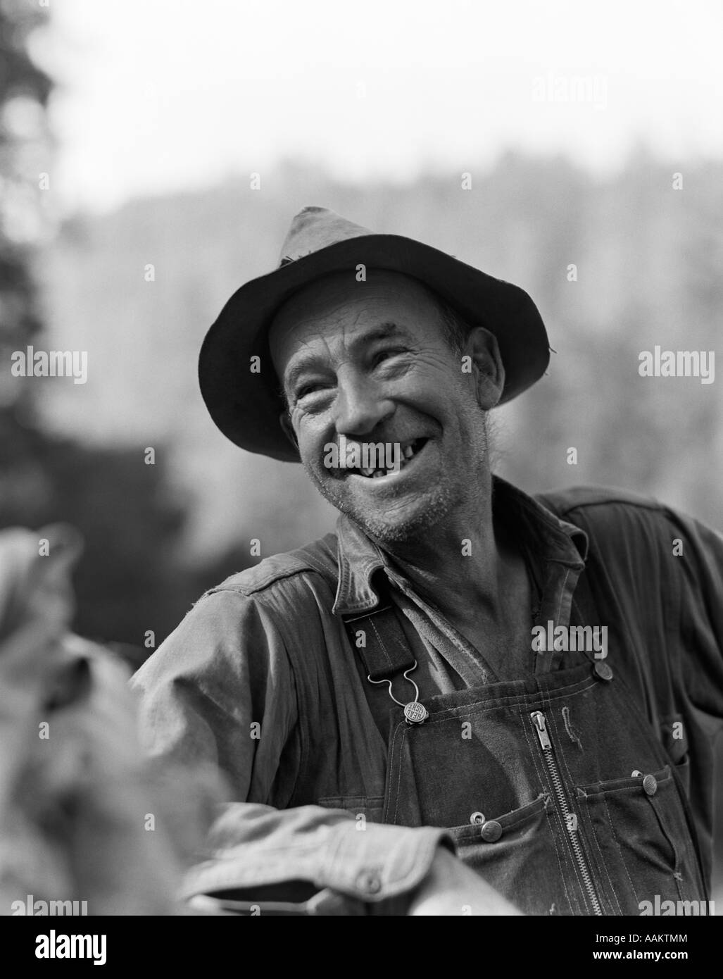 1930ER JAHREN LÄCHELND ÄLTEREN GOLDSUCHER AN SMITH RIVER CALIFORNIA FEHLENDE ZÄHNE TRAGEN OVERALLS UND HUT Stockfoto