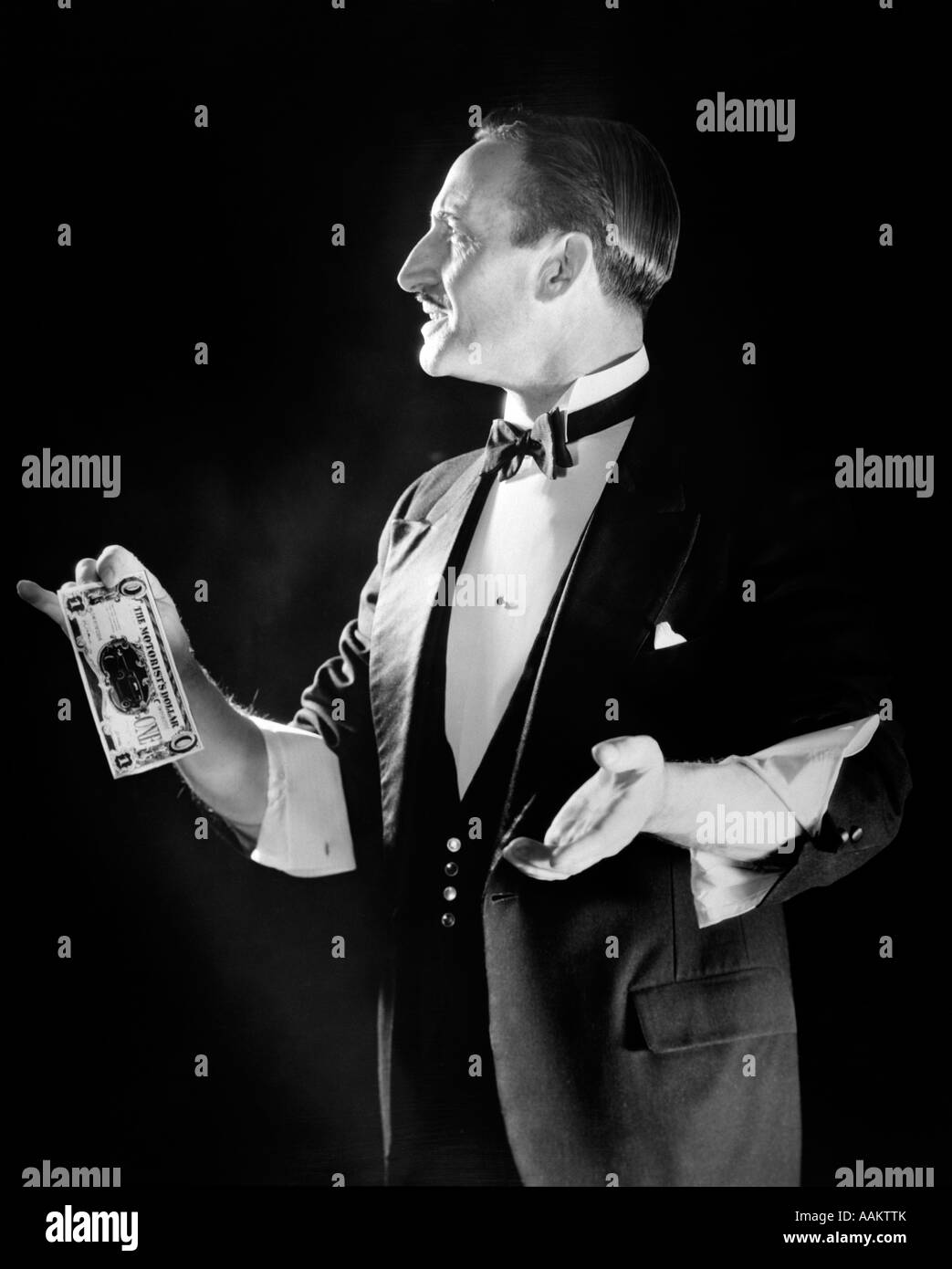 1920ER JAHREN MAGIER IN SMOKING MIT ÄRMELN AUFGEROLLT IN DER HAND AUS DOLLARSCHEIN Stockfoto