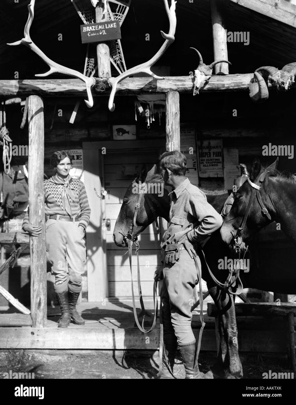1920S 1930S LODGE PAAR UND PFERDE VOR WESTLICHEN JAGD VERANDA MIT TROPHÄE GEWEIH SCHÄDEL BRAZEAU LAKE ALBERTA Stockfoto