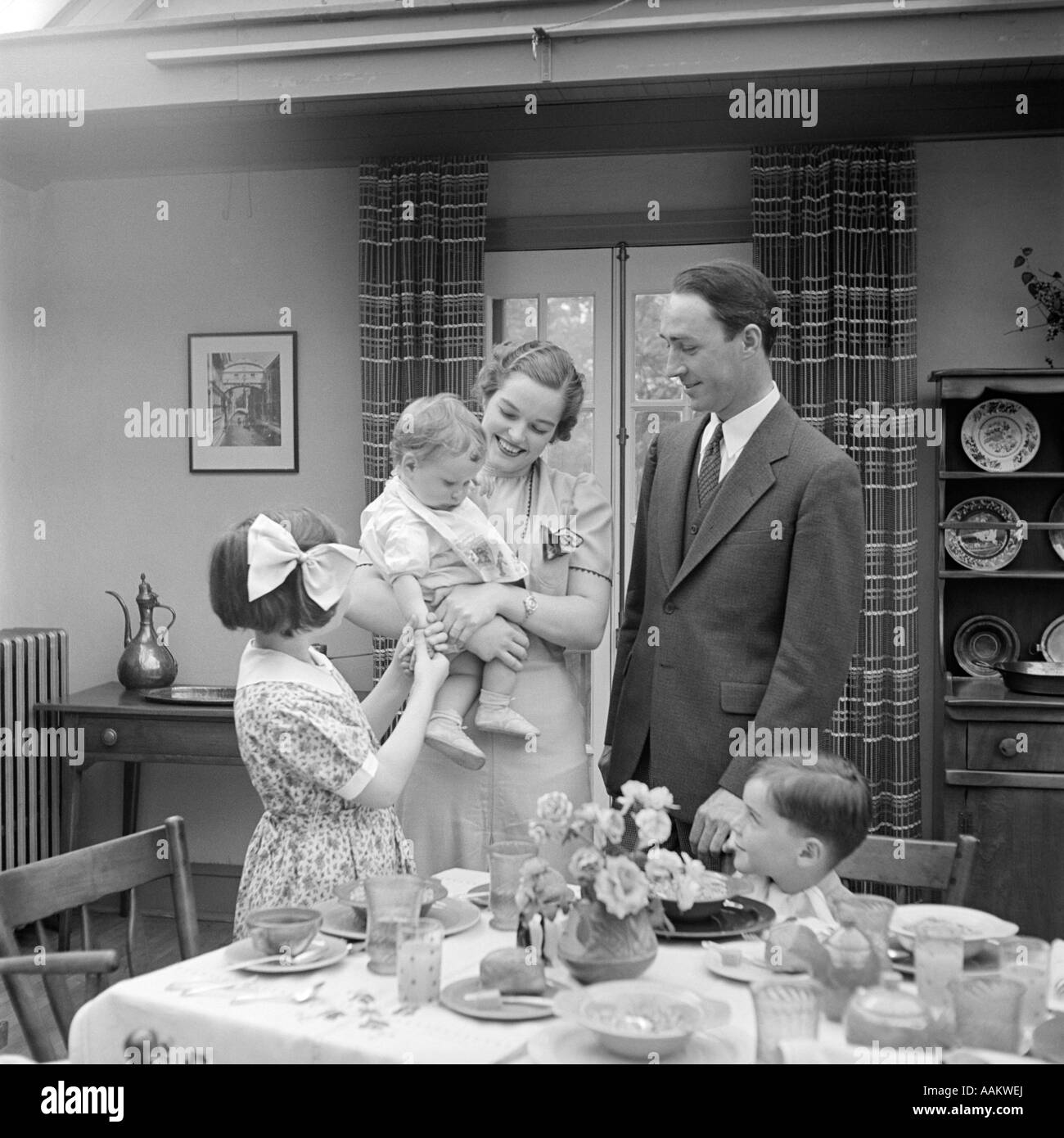 1930ER JAHRE FAMILIE VON 5 IM SPEISESAAL MUTTER STEHEND HOLDING BABY Stockfoto