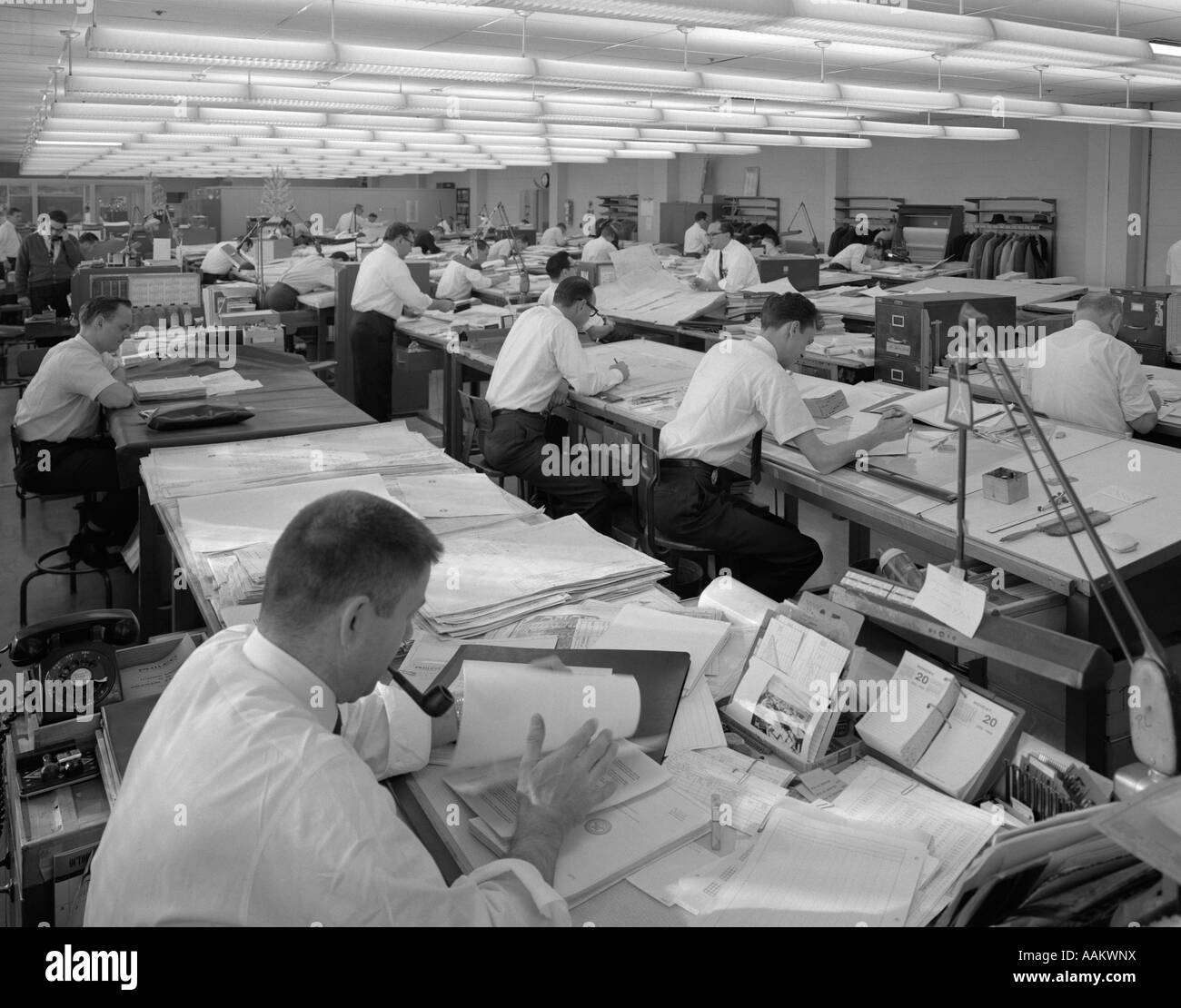1960ER JAHREN MÄNNER SITZEN AN AUSARBEITUNG TISCHEN ARBEITEN IN GROßEN LEUCHTSTOFFLAMPE BELEUCHTET ENGINEERING BÜRO/PRAXISFLÄCHEN Stockfoto