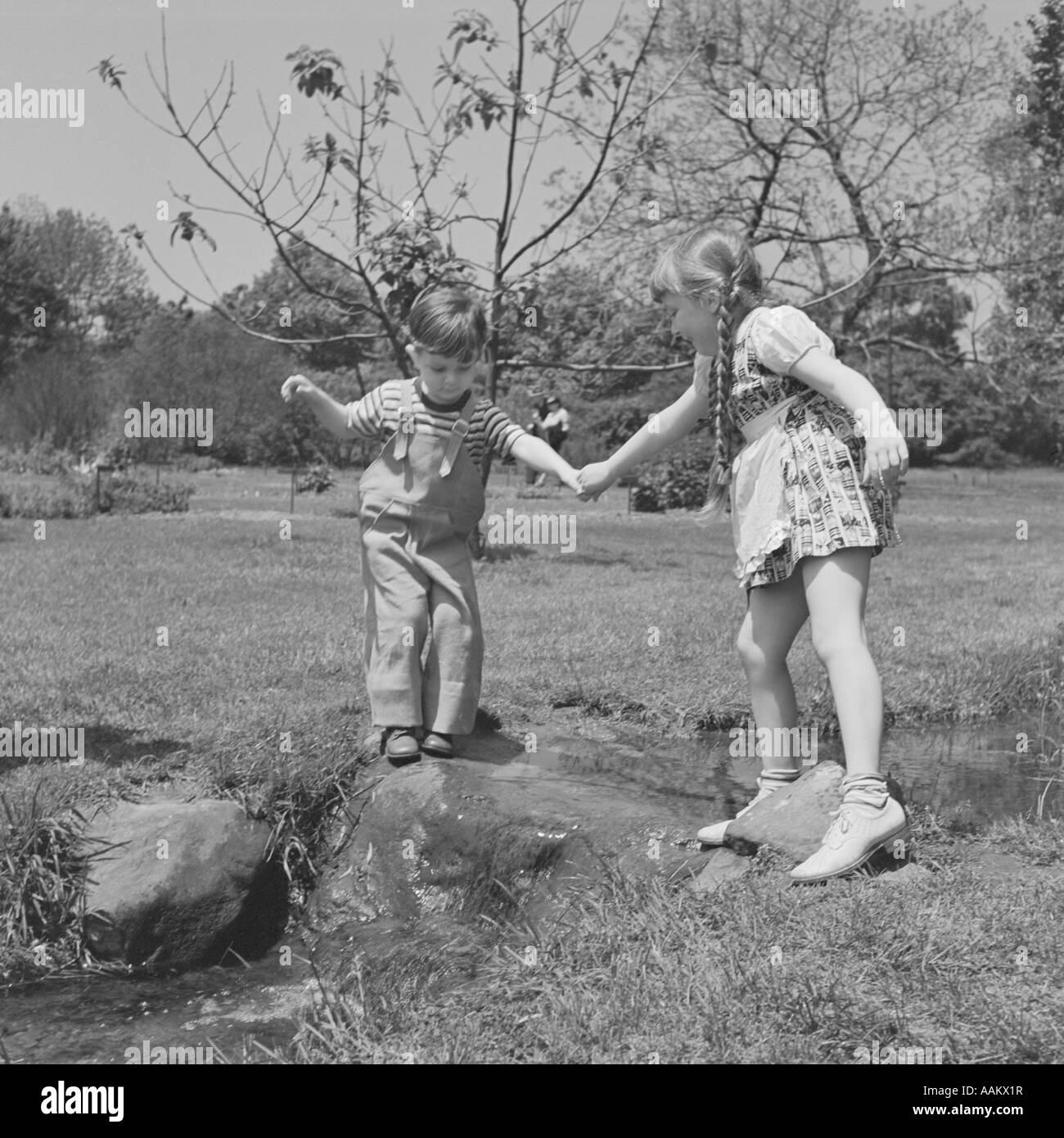 1950ER JAHRE MÄDCHEN HELFEN JÜNGEREN KNABEN ÜBER BACH Stockfoto