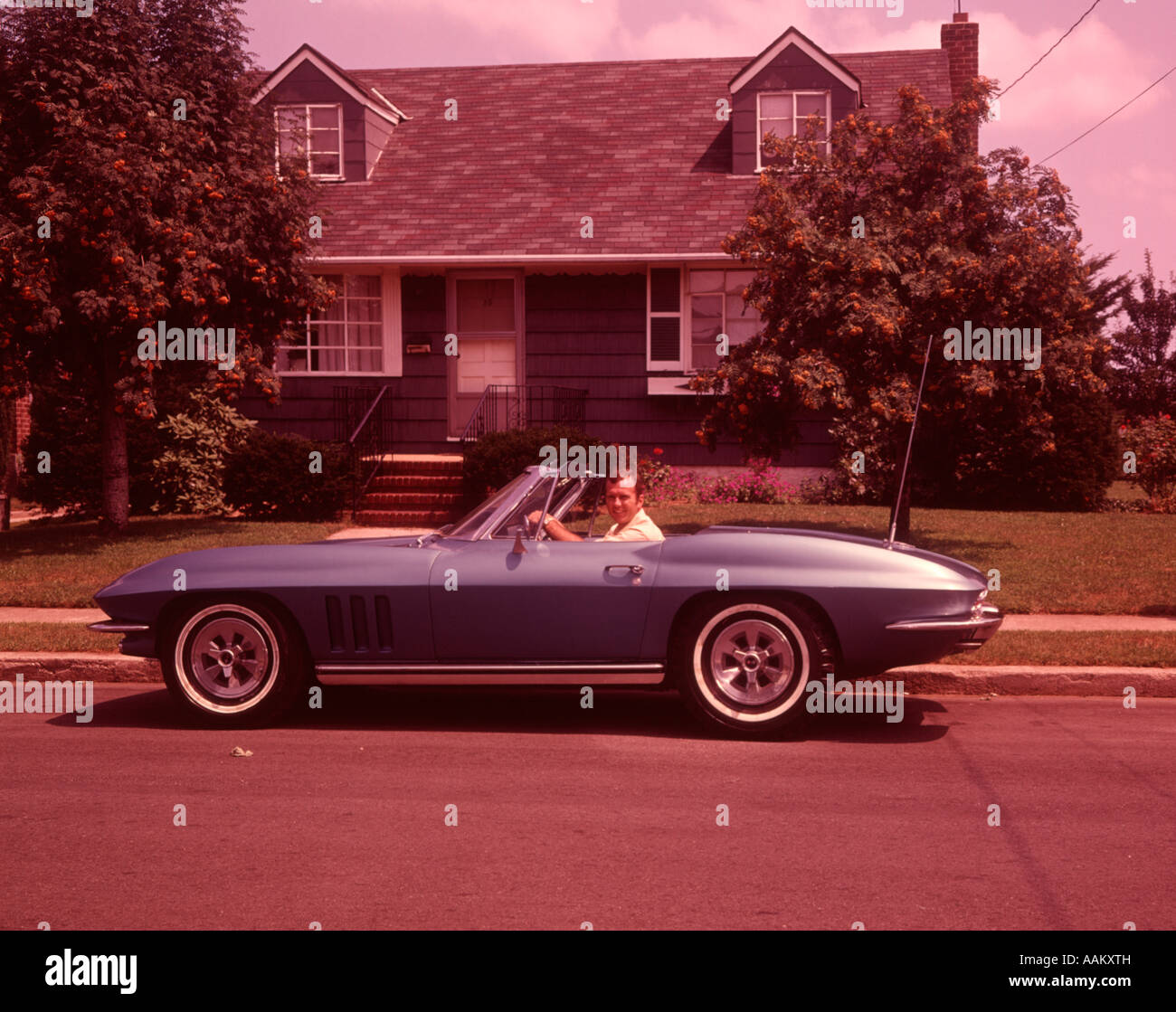 1960ER JAHRE MANN IN CORVETTE CABRIO VOR HAUS Stockfoto