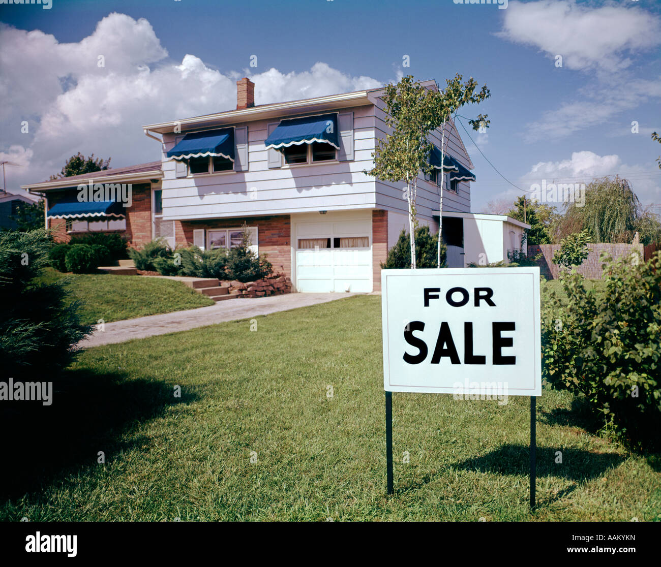 1960ER JAHREN SPLIT LEVEL RANCH HAUS HAUS MIT FÜR VERKAUF ZEICHEN VORGARTEN RASEN Stockfoto