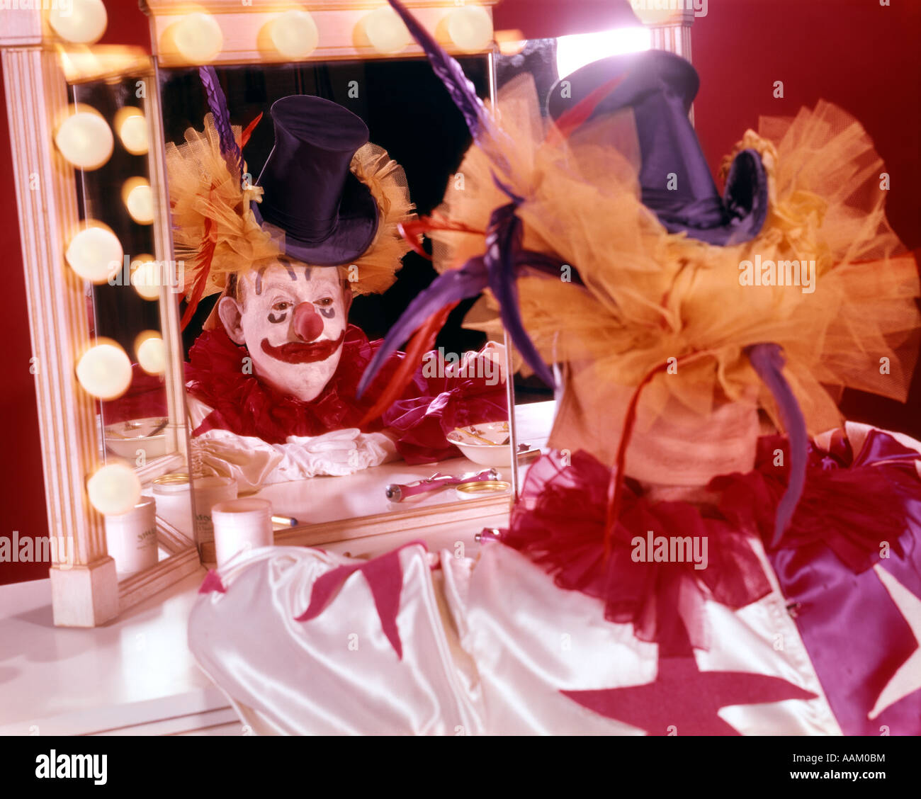 1970ER JAHRE MANN GEKLEIDET ALS CLOWN SITZT AN MAKE-UP SPIEGEL REFLEXION HUT Stockfoto