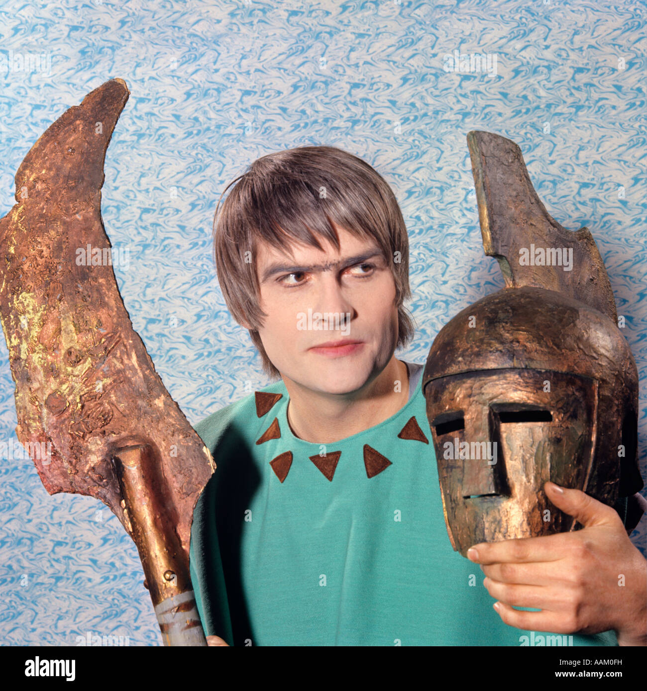 1970ER JAHRE MANN SCHAUSPIELER KOSTÜM GRIECHISCHE TRAGÖDIE BLICK AUF SEITE HÄLT MASKE HELM KLINGE LANCE Stockfoto