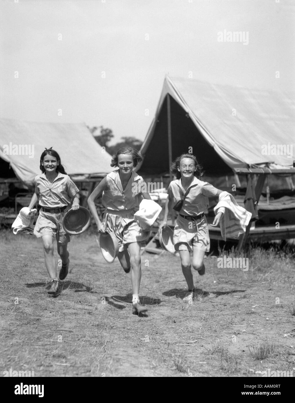 1930ER JAHREN DREI TEEN MÄDCHEN TRAGEN CAMP SHORTS & SHIRTS VON ZELTEN MIT GEDRÜCKTER HANDTÜCHER & WASCHBECKEN LAUFEN Stockfoto