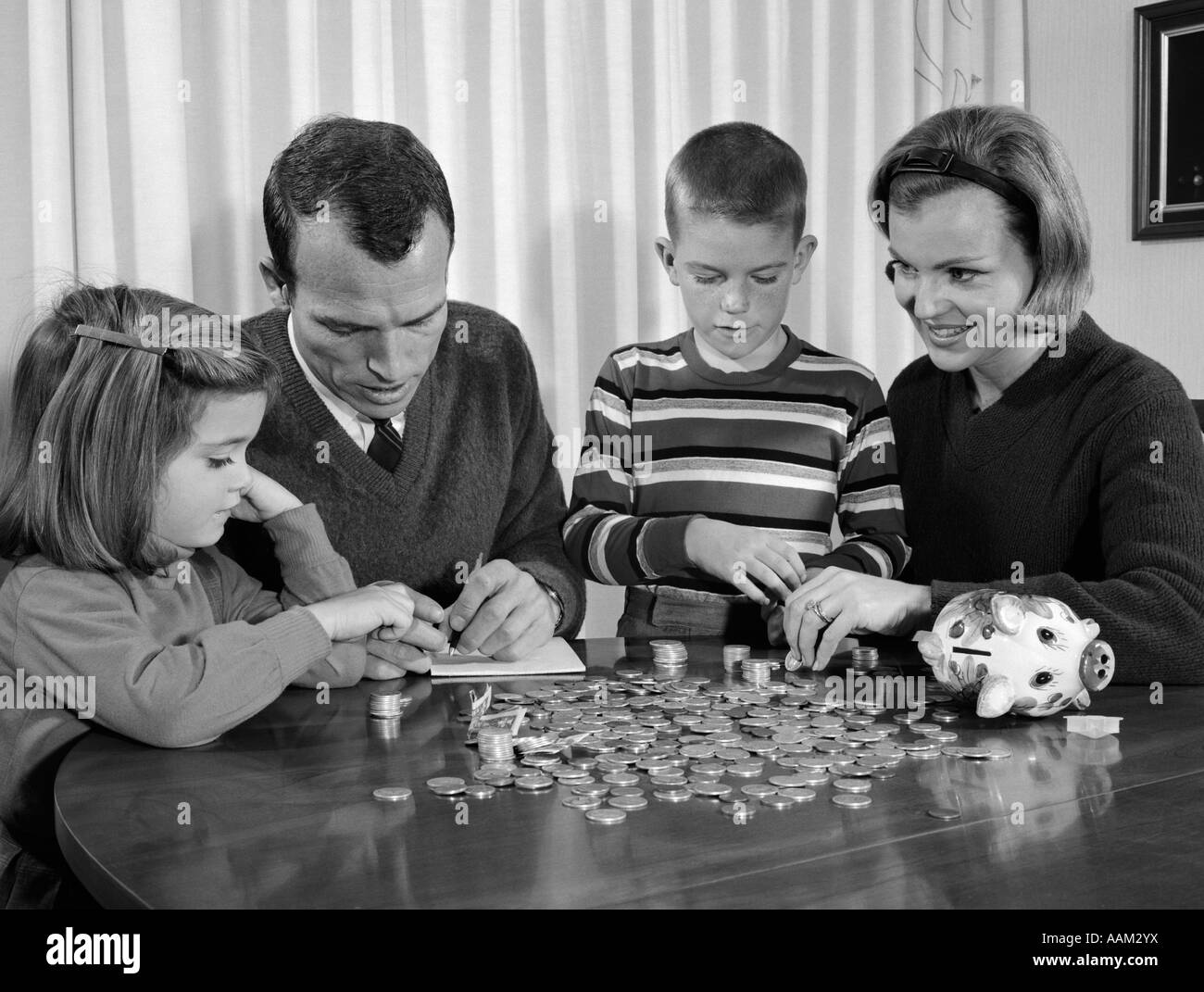 1960ER JAHREN ELTERN SITZEN AM ESSTISCH MIT TOCHTER & SOHN ZÄHLEN WECHSEL VON SPARSCHWEIN Stockfoto