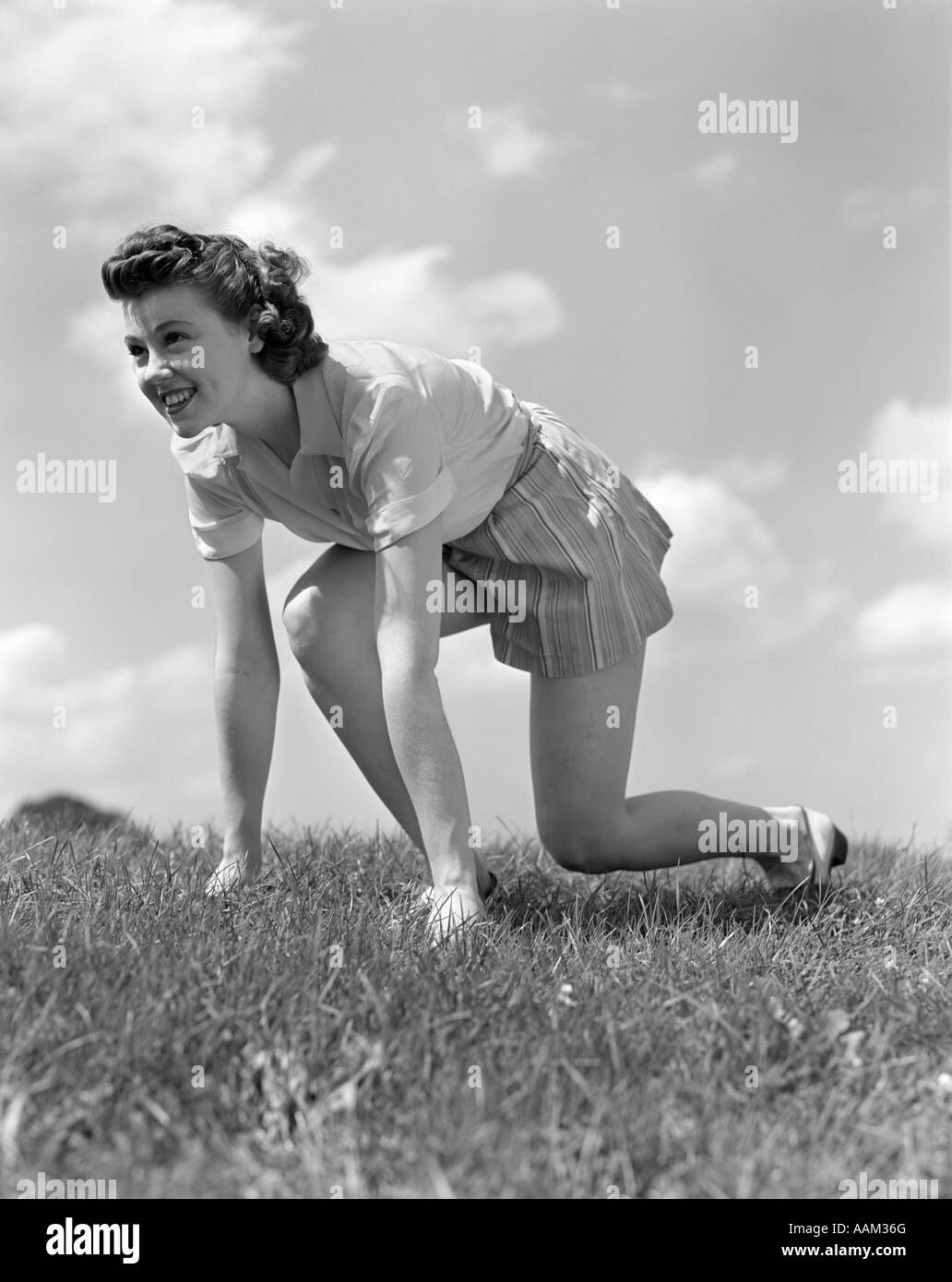 1940ER JAHRE LÄCHELNDE JUNGE TEEN FRAU KNIEND IM GRASS IN TRACK RENNEN BEREIT STARTPOSITION Stockfoto
