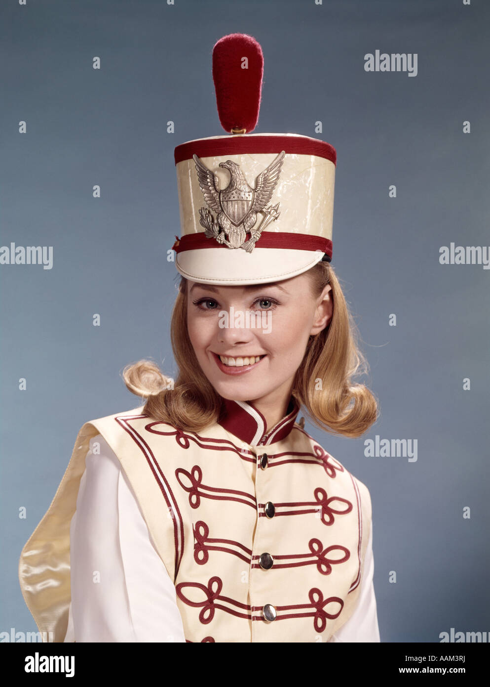 1960ER JAHREN LÄCHELND BLONDE FRAU TEEN IN BAND EINHEITLICHEN HUT MIT FEDER BRAID BRASS EAGLE MAJORETTE MUSIK MÄRZ PARADE Stockfoto