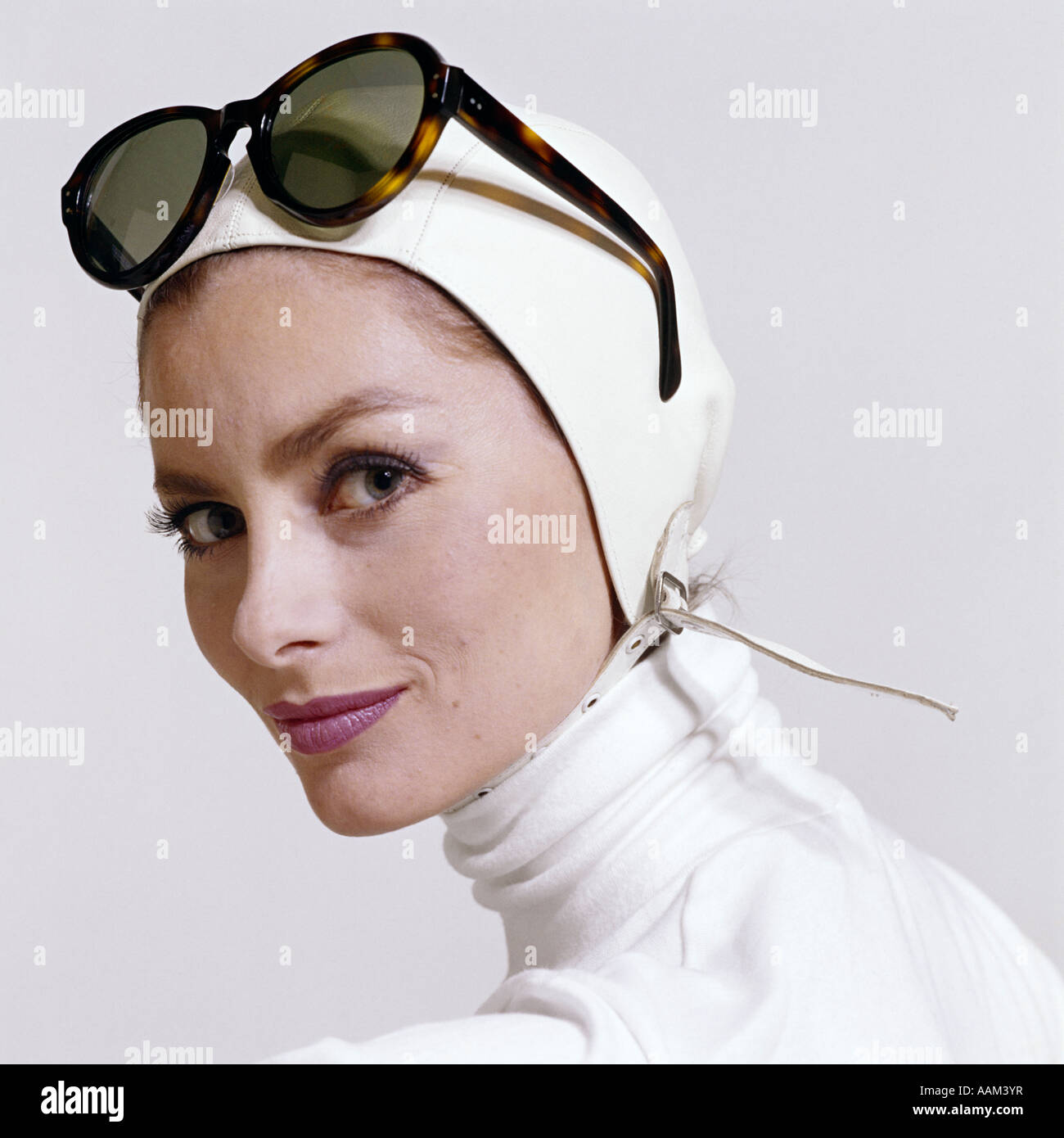 1970ER JAHREN PROFIL LÄCHELNDE FRAU MIT DESIGNERMODE WEIßE SCHILDKRÖTE HALS WEIß SPITZENLEDER AVIATOR HELM GROß SCHILDPATT Stockfoto