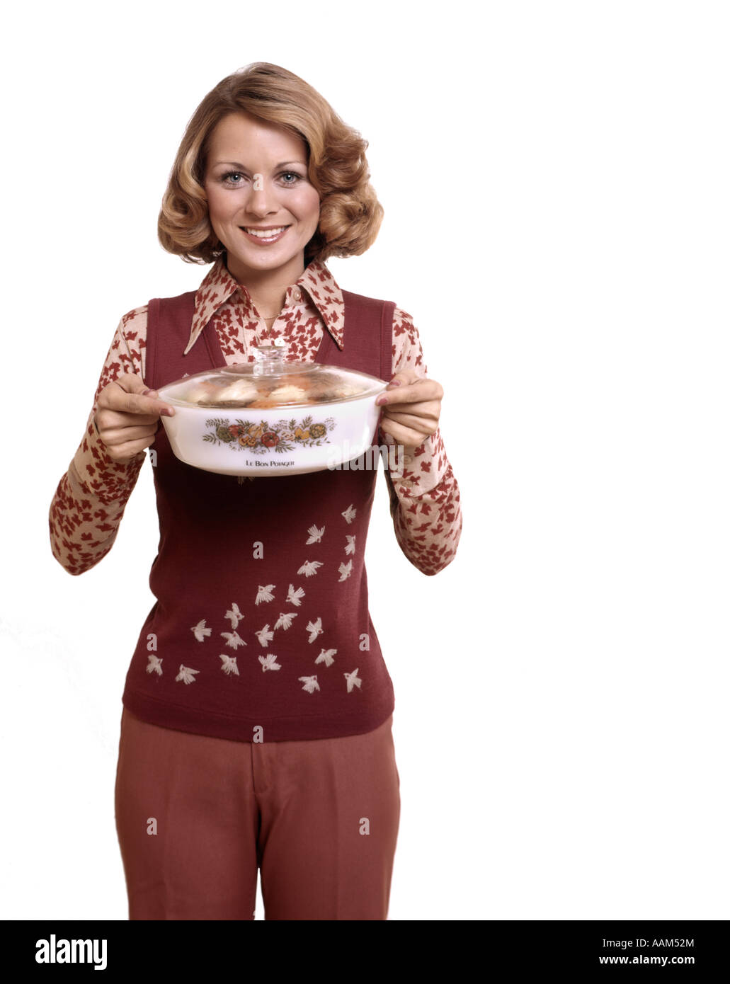 1970ER JAHREN FRAU HAUSFRAU STOLZ HALTEN UND PRÄSENTIEREN BEDECKTEN TELLER EINTOPF KOCHEN Stockfoto