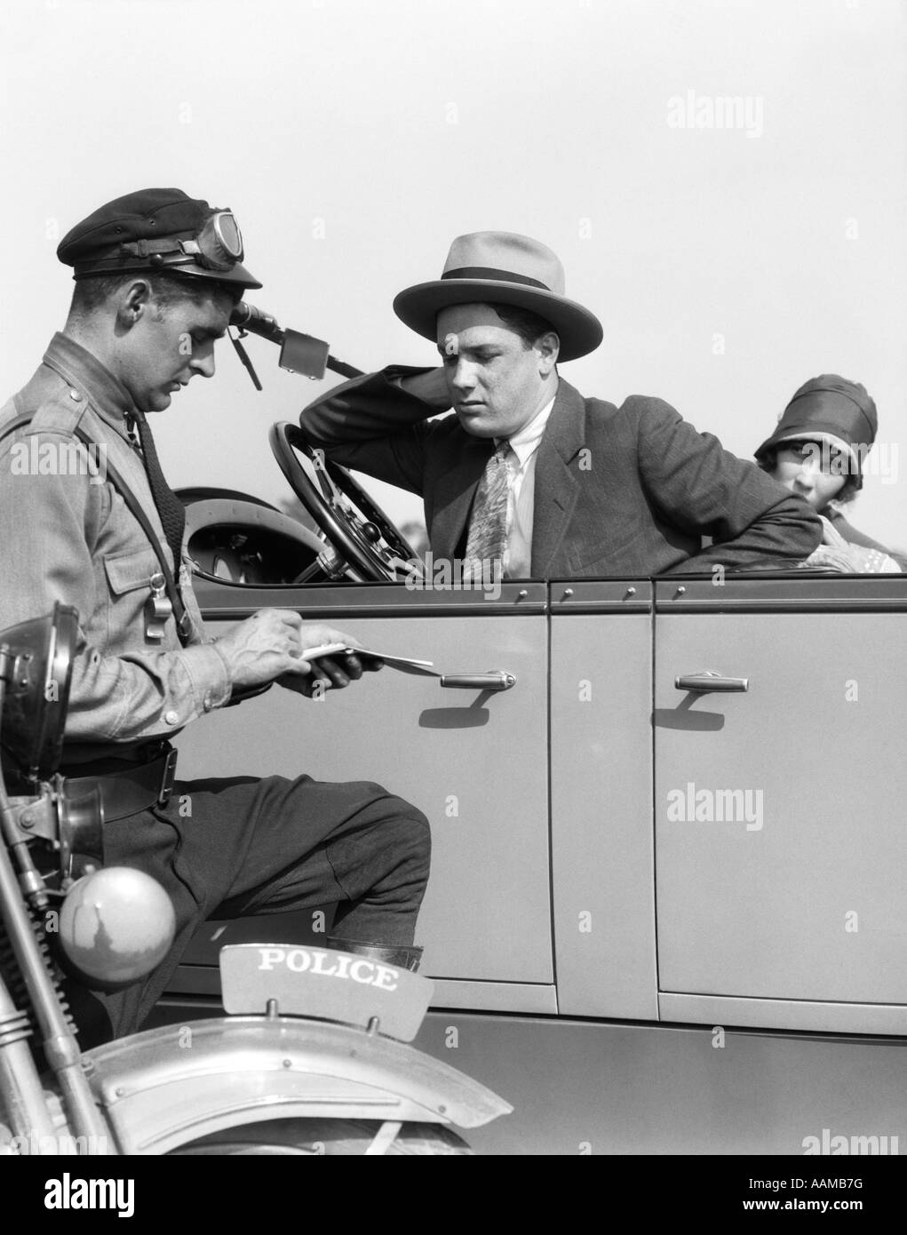 1920ER JAHREN MOTORRAD POLIZIST SCHREIBEN A SPEEDING TICKET EIN PAAR SITZEN IN CABRIOLIMOUSINE Stockfoto