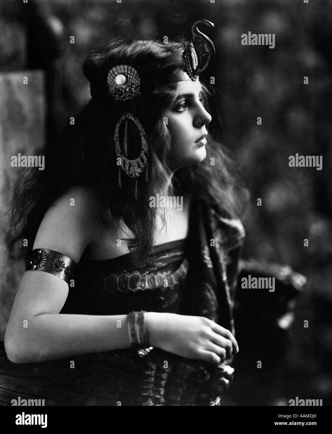 1910S 1920S FRAU IN ÄGYPTISCHEN AUSSEHENDE KOSTÜM TRÄGT JEWELED ARM MANSCHETTE & VERZIERTEN KOPF STÜCK MIT SNAKE AUF VORDERSEITE Stockfoto