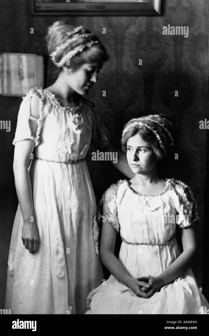 1890S 1900 WENDE DES JAHRHUNDERTS PAAR JUNGE FRAUEN SCHWESTERN MIT GIRLANDEN IN HAAR PASSENDEN STUTZEN AUF KLEIDER Stockfoto