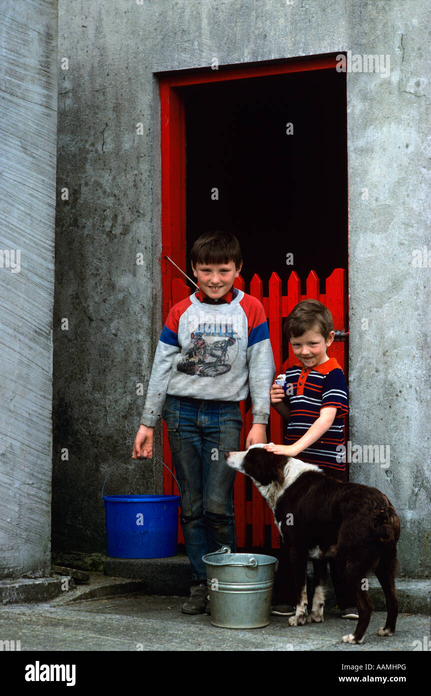 ZWEI JUNGEN MIT ROTEN SCHEUNENTOR MIT EIMERN UND HUND KILLYBEGS COUNTY DONEGAL IRELAND Stockfoto