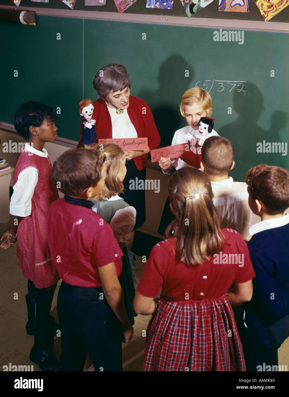 1970ER JAHREN VERSAMMELTEN SICH LEHRER UND SCHÜLER ZEIGT HANDPUPPEN ZU KLASSENKAMERADEN UM SIE HERUM Stockfoto