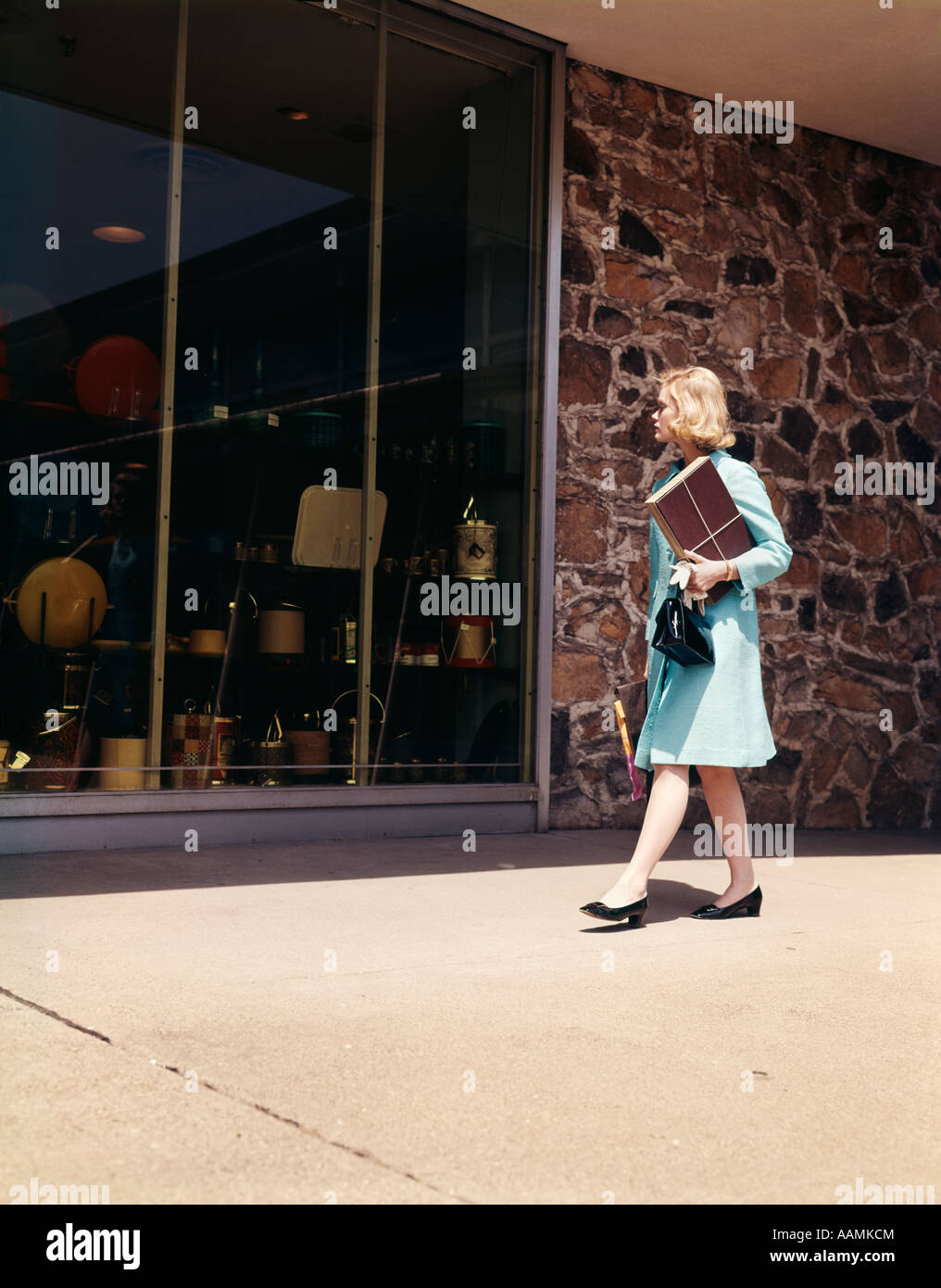 1960 1960S BLONDE FRAU BLUE COAT WALKING DOWN STREET SCHAUFENSTERBUMMEL AUF DER SUCHE IM SHOP SHOP WINDOWS EINZELHANDEL RETRO Stockfoto