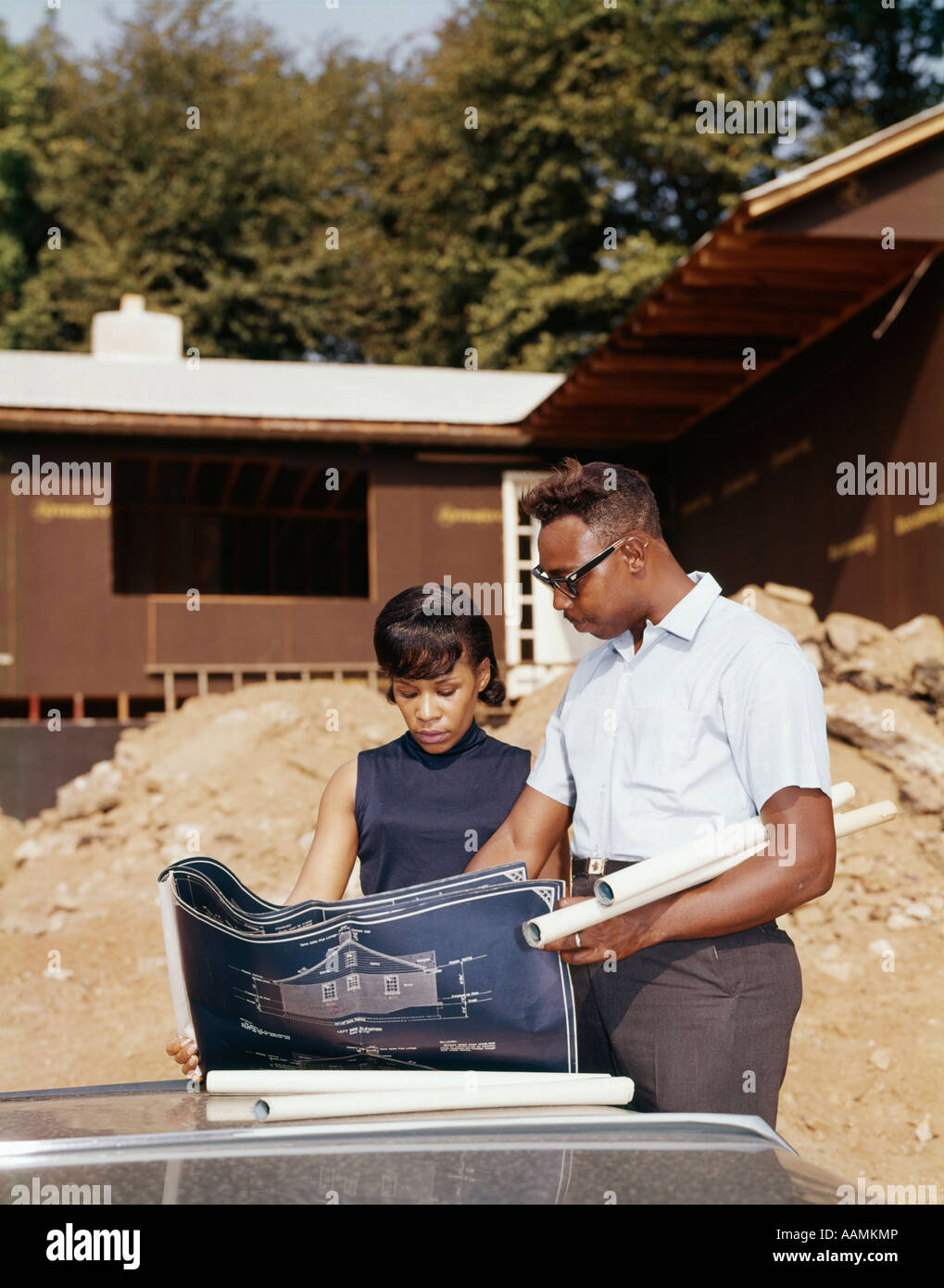 1960ER JAHREN AFROAMERIKANISCHEN PAAR BLICK AUF BLAUPAUSE PLÄNE FÜR NEUES HAUS IM BAU Stockfoto