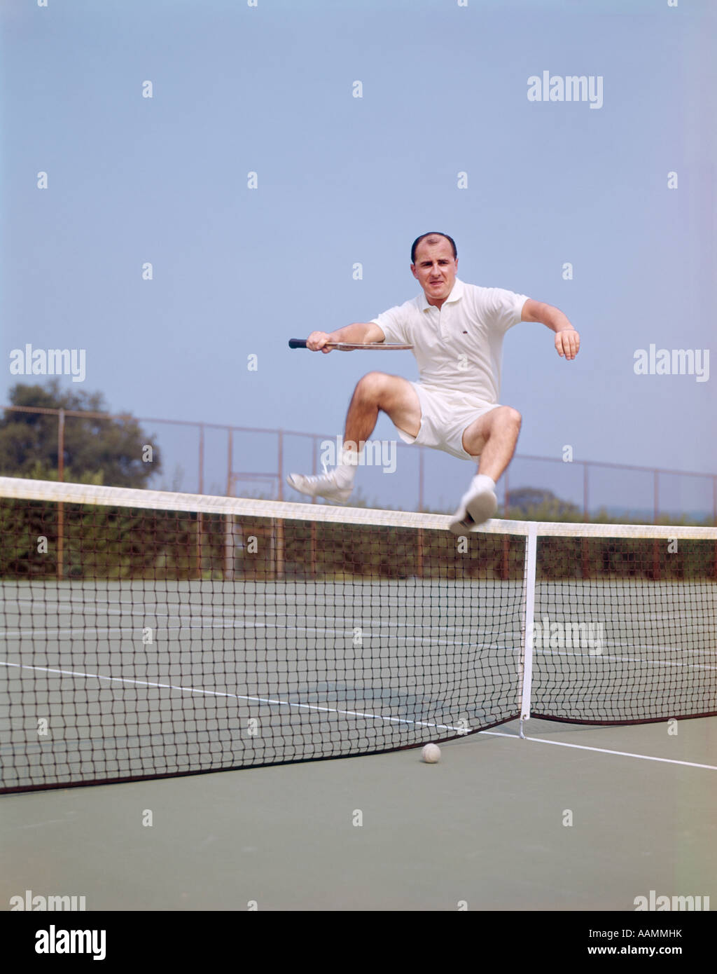 MITTE DER 1970ER-JAHRE ALTER MANN SPRINGT ÜBER NETZ AUF TENNISPLATZ GLATZENBILDUNG FITNESS AGILE WELLNESS LIFESTYLE Stockfoto