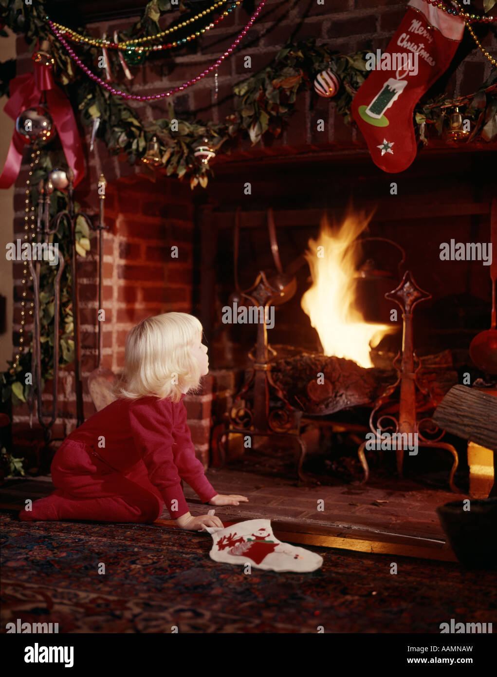 1960ER JAHREN KLEINE BLONDE MÄDCHEN KAMIN DEKORIERT FÜR WEIHNACHTEN HALTEN STRUMPF NOSTALGIE SANTA Stockfoto