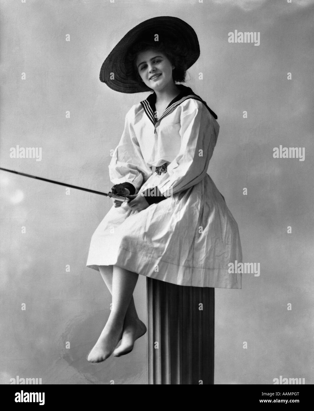 1910S 1920S TRAGEN DAMENKLEID MIT SEEMANN STIL KRAGEN STROH HUT SITZT AUF POST MIT ANGELRUTE Stockfoto