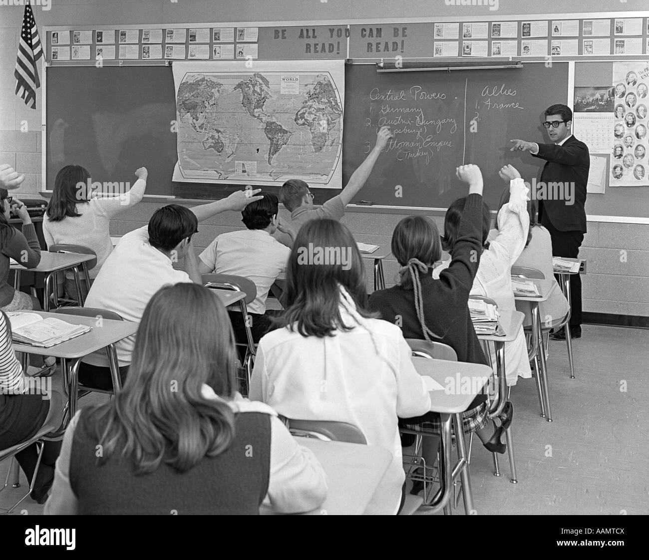 1970ER JAHREN LEHRER AUF ERHOBENEN HAND TEEN KLASSENZIMMER STUDENTEN GESEHEN VON HINTEN AUSSEHEN TAFEL KARTE WELTKLASSE-GESCHICHTE Stockfoto