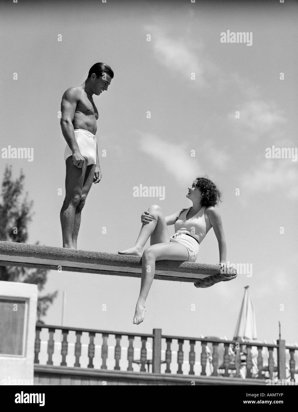 1930ER JAHREN PAAR AM SWIMMING POOL SPRUNGBRETT IM GESPRÄCH Stockfoto