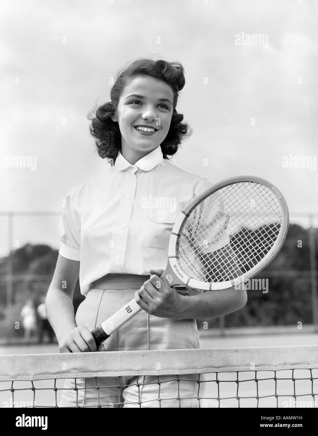 1950S 1940S FRAU POSIERT MIT TENNISSCHLÄGER AM TENNISPLATZ IN DER NÄHE VON NET Stockfoto