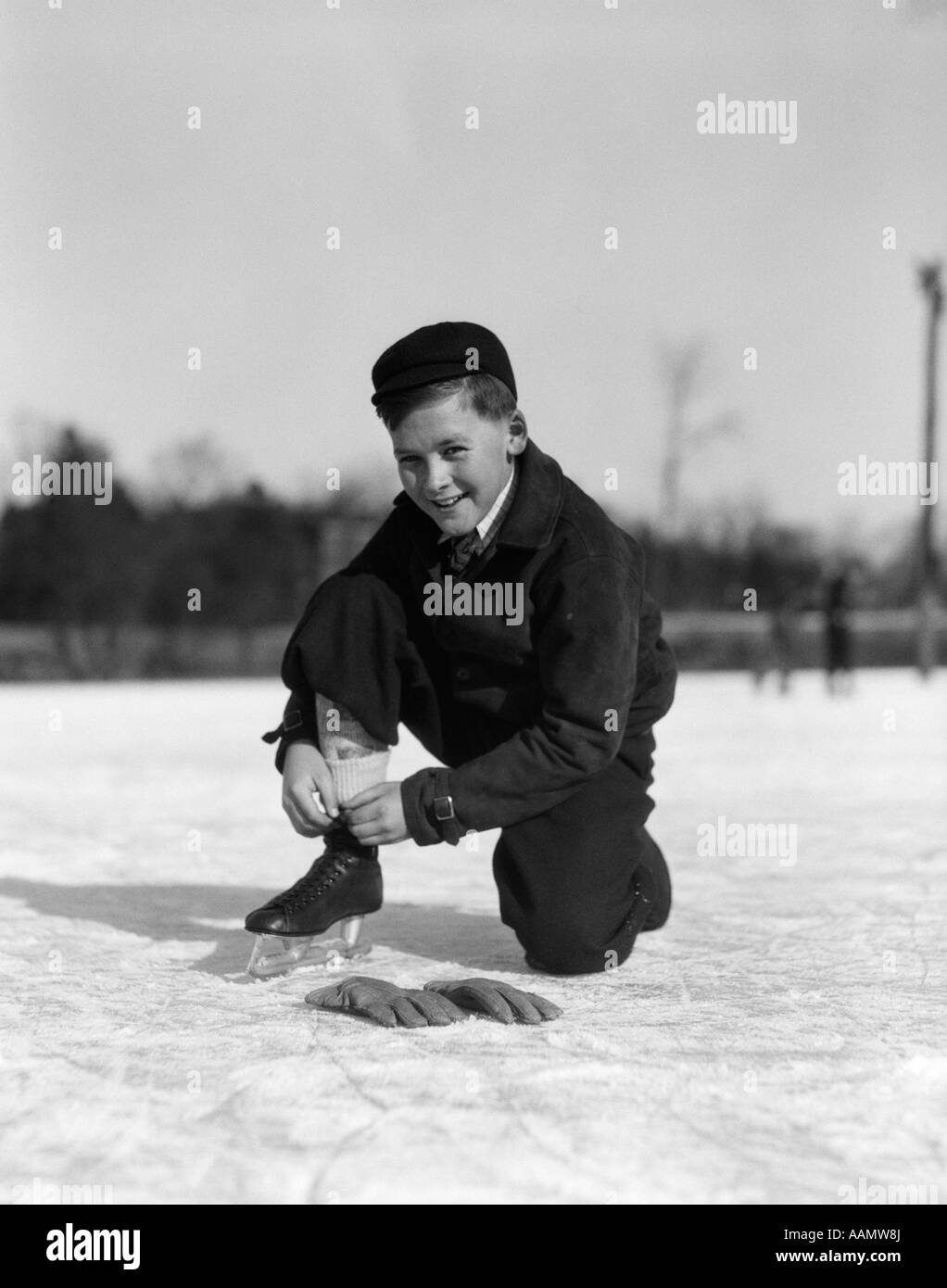 1930ER JAHRE JUNGE BINDEN ICE SKATE LACE KNIEND AUF DEM EIS, BLICK IN DIE KAMERA Stockfoto