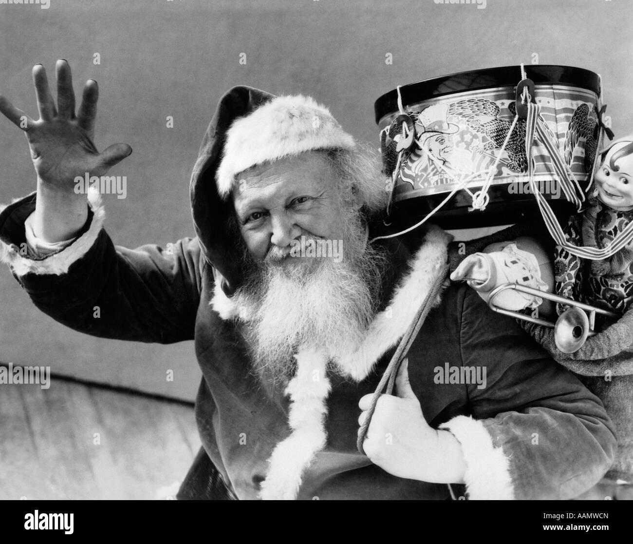 1930ER JAHREN SANTA CLAUS HOLDING TASCHE GESCHENKE SPIELZEUG TROMMEL PUPPEN WINKEN, BLICK IN DIE KAMERA Stockfoto