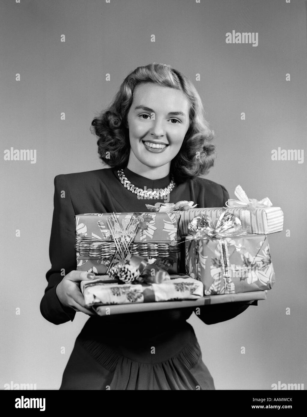 1950ER JAHREN LÄCHELNDE FRAU HOLDING HAUFEN VERPACKTE WEIHNACHTSGESCHENKE BLICK IN DIE KAMERA Stockfoto