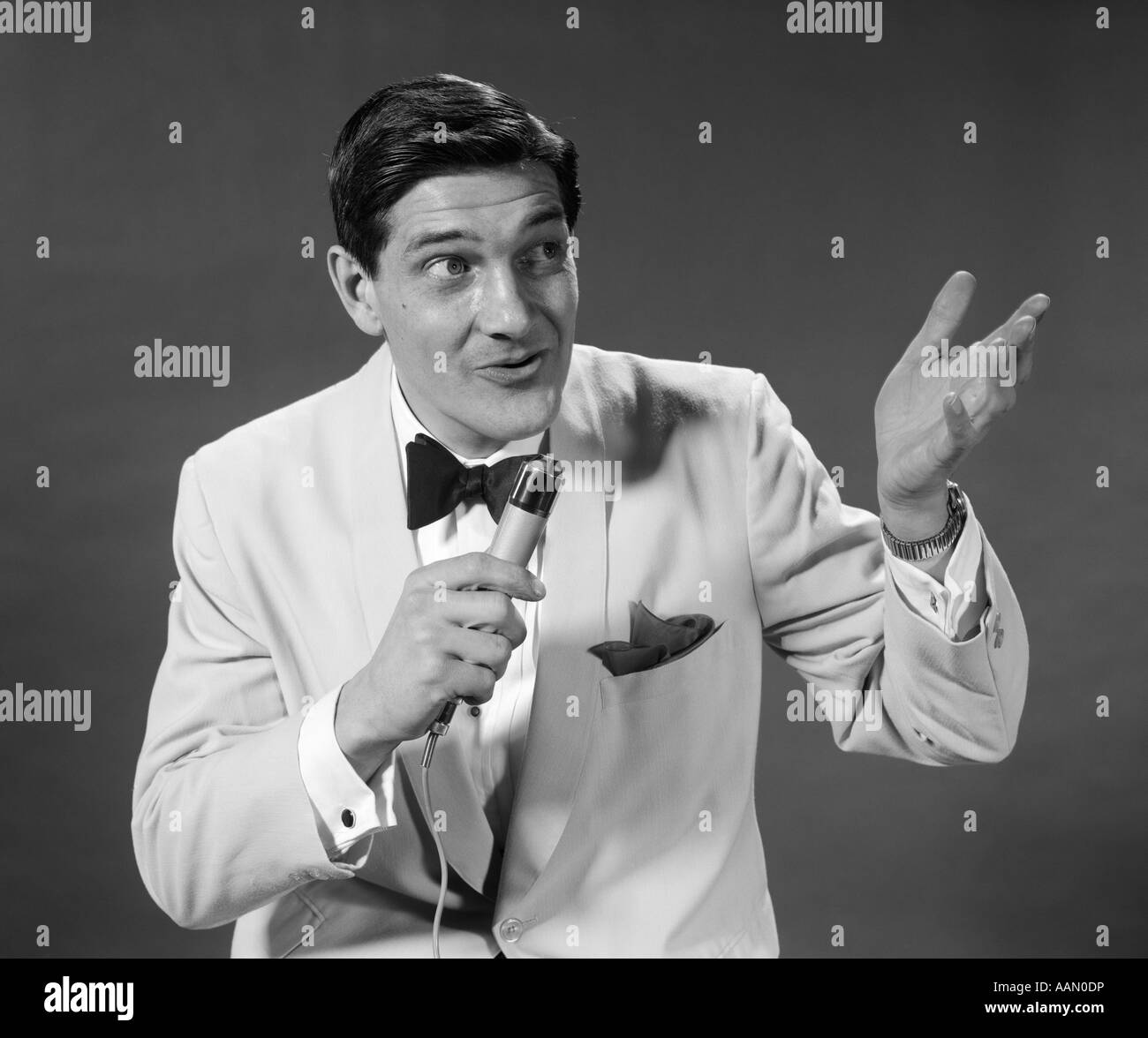 1950S 1960S MANN WEIßE SMOKINGJACKE HALTEN MIKROFON SINGEN TALK GESTE MIT HAND PERFORMER HOST CONFERENCIER Stockfoto
