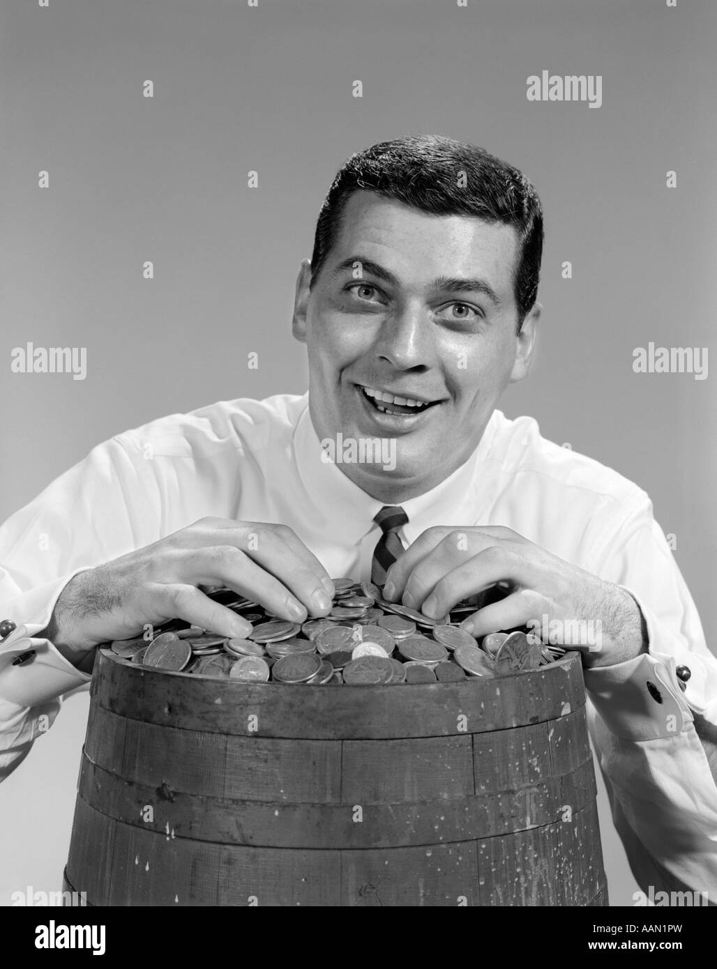 1960ER JAHRE LUSTIGES GESICHT AUSDRUCK LÄCHELND MANNHÄNDE AUF FASS VOLLER MÜNZEN GELD JACKPOT FINANZEN GEWINNEN LOTTERIE Stockfoto