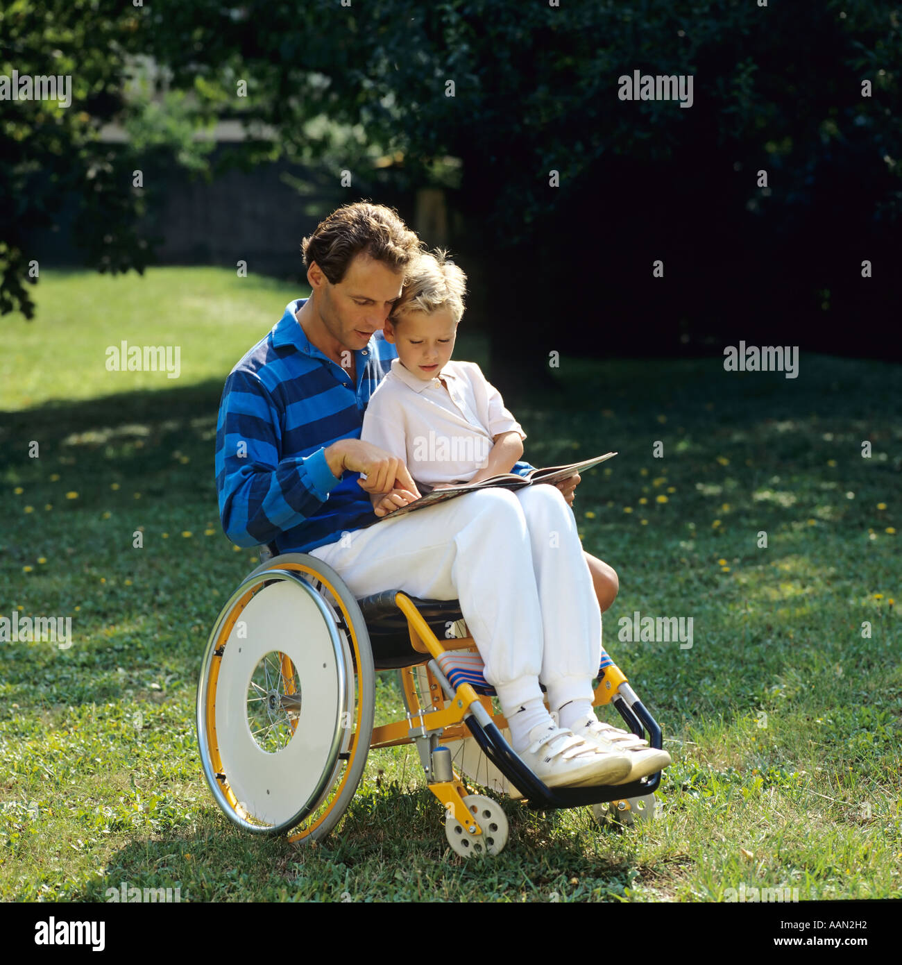 Behinderter im Rollstuhl liest einem kleinen Jungen im Garten ein Buch vor Stockfoto