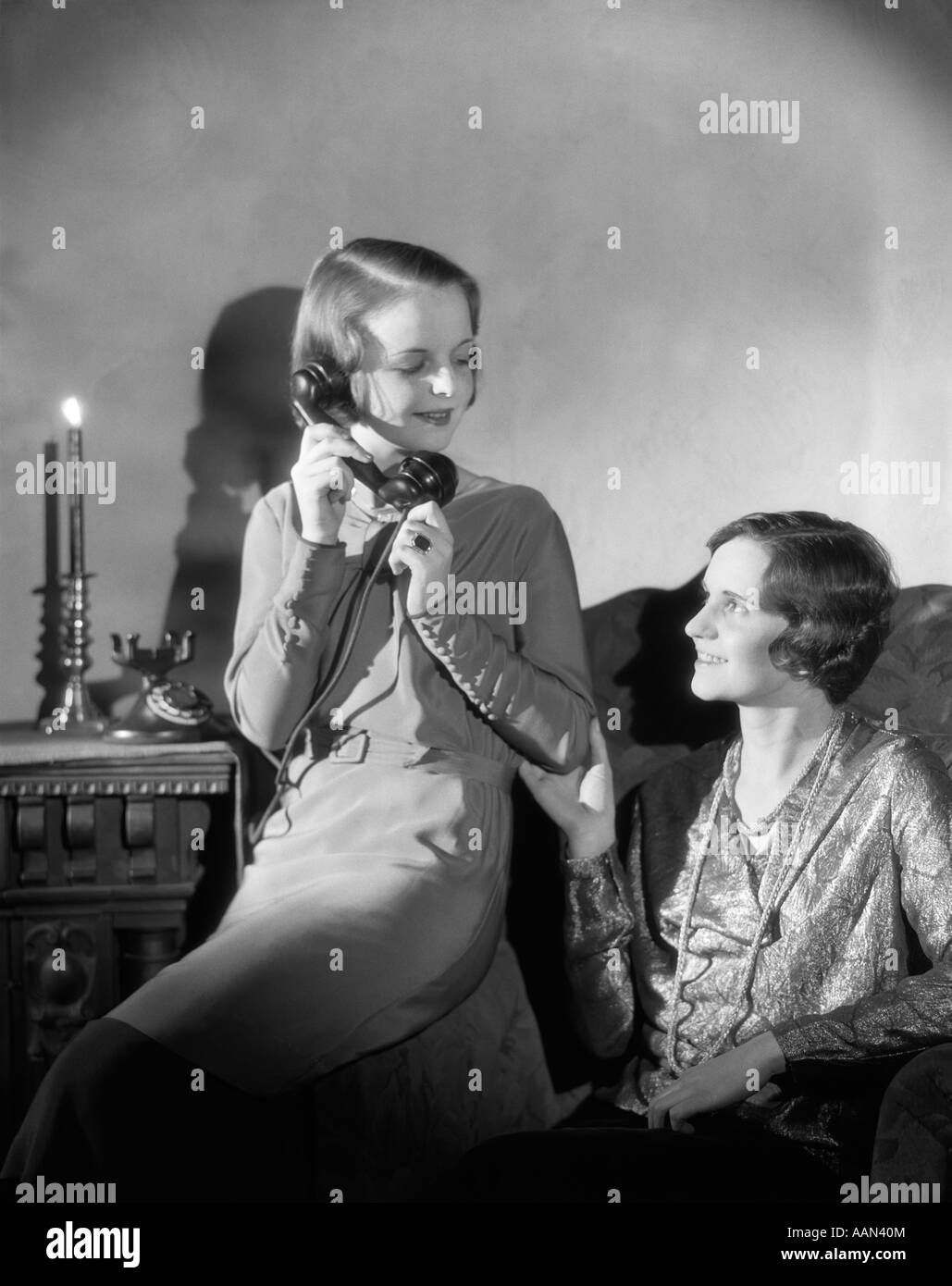 1920S 1930S TELEFON ZWEI FRAUEN EIN GESPRÄCH AUF ANDERE SITZEN IM STUHL CANDLE-LIGHT Stockfoto