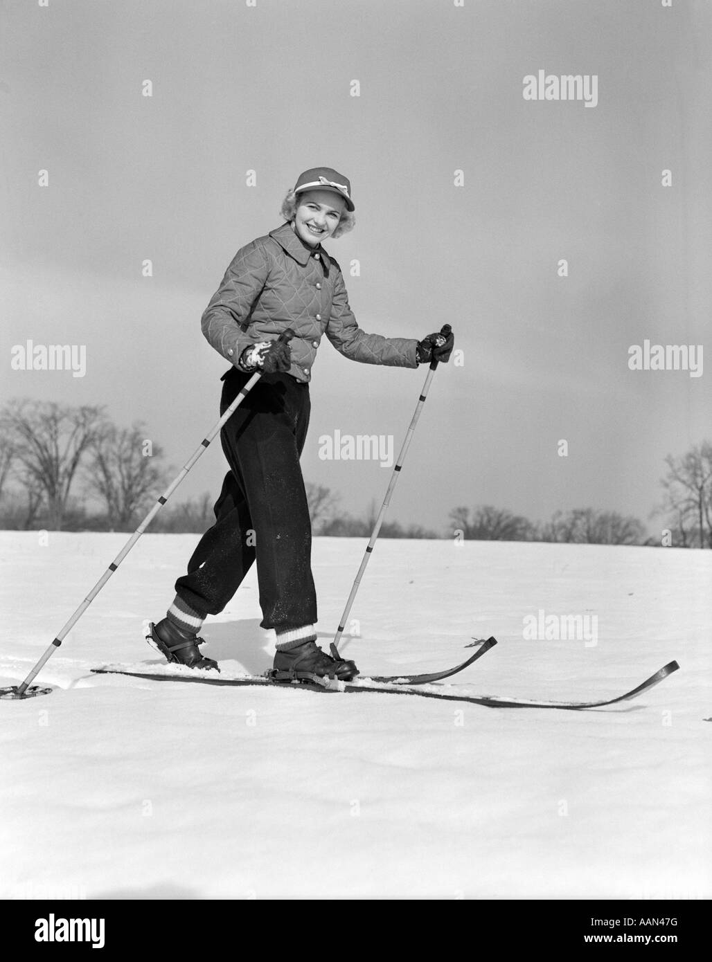 1940ER JAHREN DER 1950ER JAHRE FRAU LÄCHELND BLICK IN DIE KAMERA MIT BAMBUS HOLZ MIT SKIERN SKI POLE IN JEDER HAND TRAGEN STEPPJACKE Stockfoto