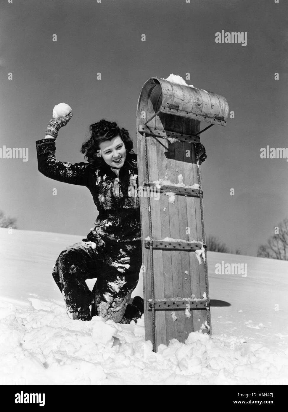 1940ER JAHREN FRAU VERSTECKT SICH HINTER RODEL SCHLITTEN MIT EINER SCHNEEBALLSCHLACHT Stockfoto