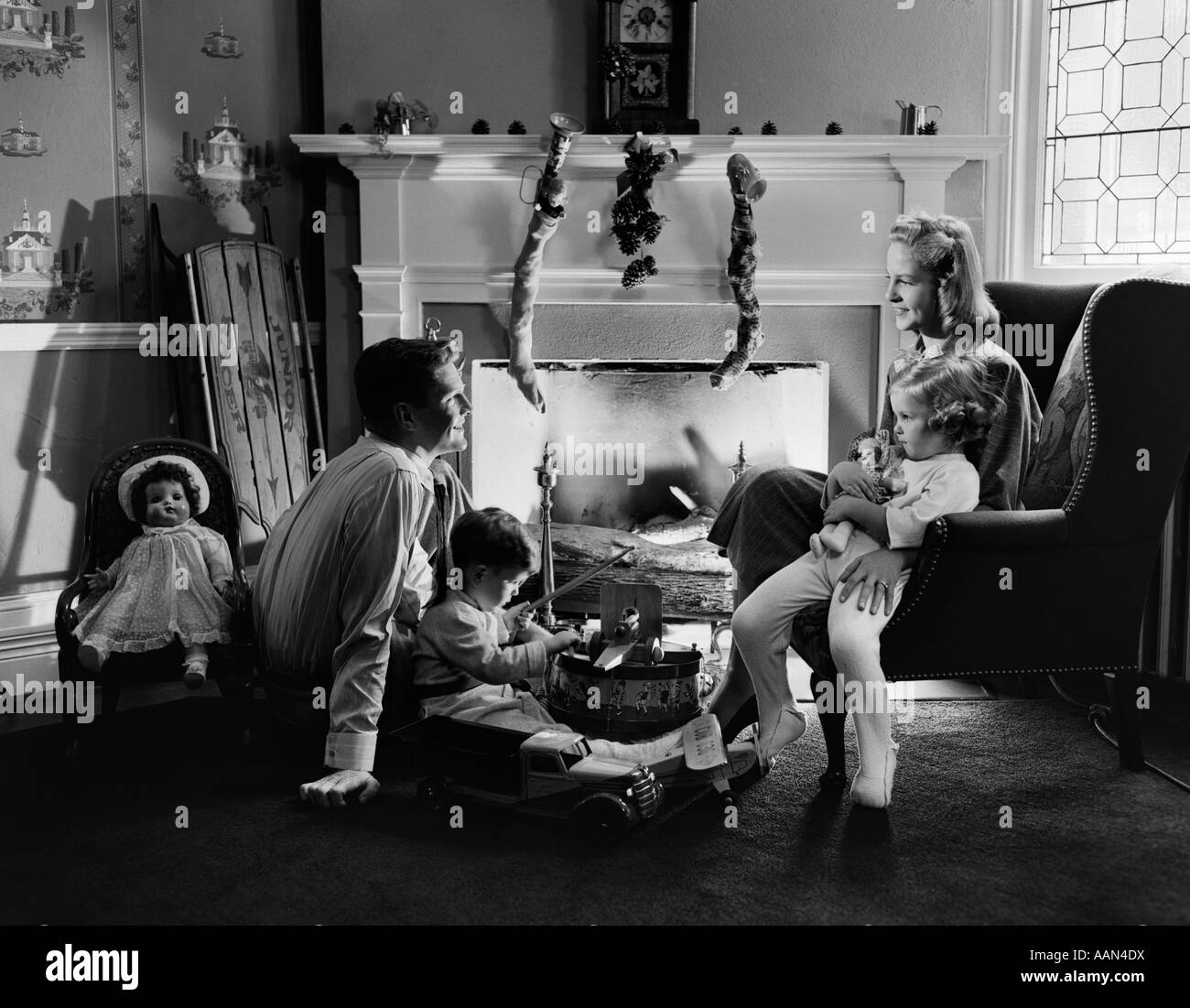 1940ER JAHRE FAMILIE SITZEN KAMIN AN WEIHNACHTEN ZEIT, DIE KINDER SPIELEN MIT SPIELZEUG Stockfoto