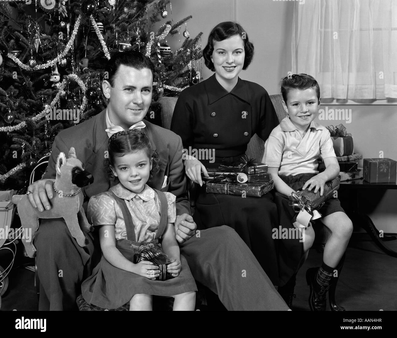 1940S 1950S FAMILIE HERUMSITZEN WEIHNACHTSBAUM HOLDING GESCHENKE BLICK IN DIE KAMERA Stockfoto