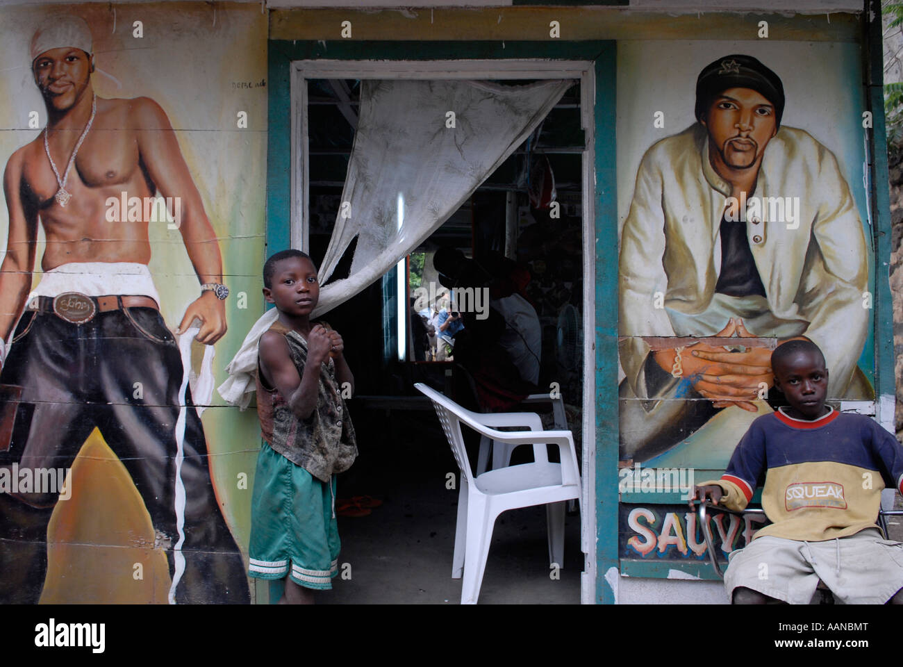 Kinder am Eingang eines Friseursalons mit handgemalten Figuren in Nord-Kivu, DR Kongo, DR Afrika Stockfoto