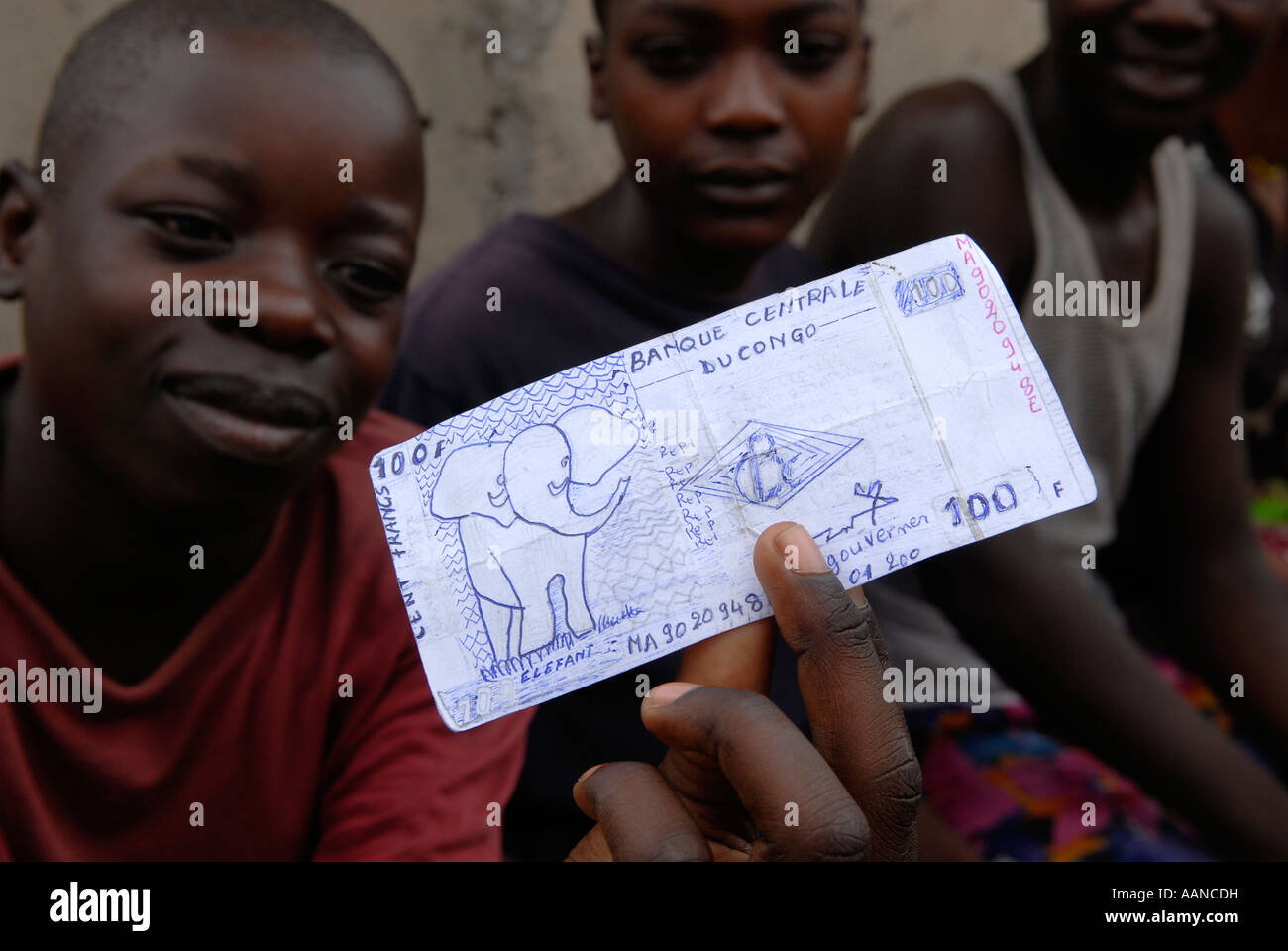 Ein ehemaliger Kindersoldat hält eine Papierzeichnung, die eine Banknote von 100 kongolesischen Franken in der Provinz Nord-Kivu in DR Kongo Afrika zeigt Stockfoto