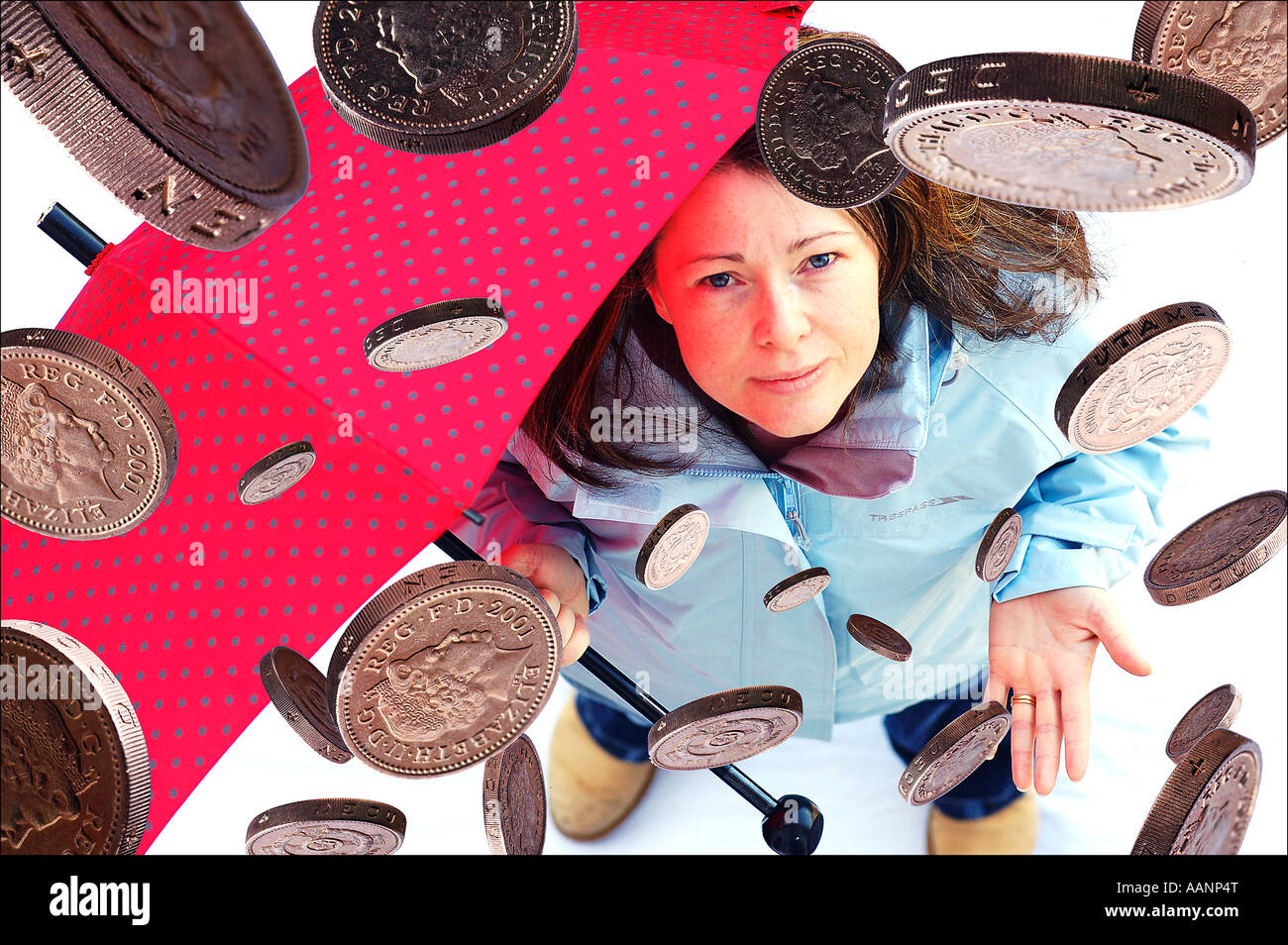 Frau (30 s) mit einem Regenschirm, während Pfund (UK)-Münzen vom Himmel fallen. Stockfoto