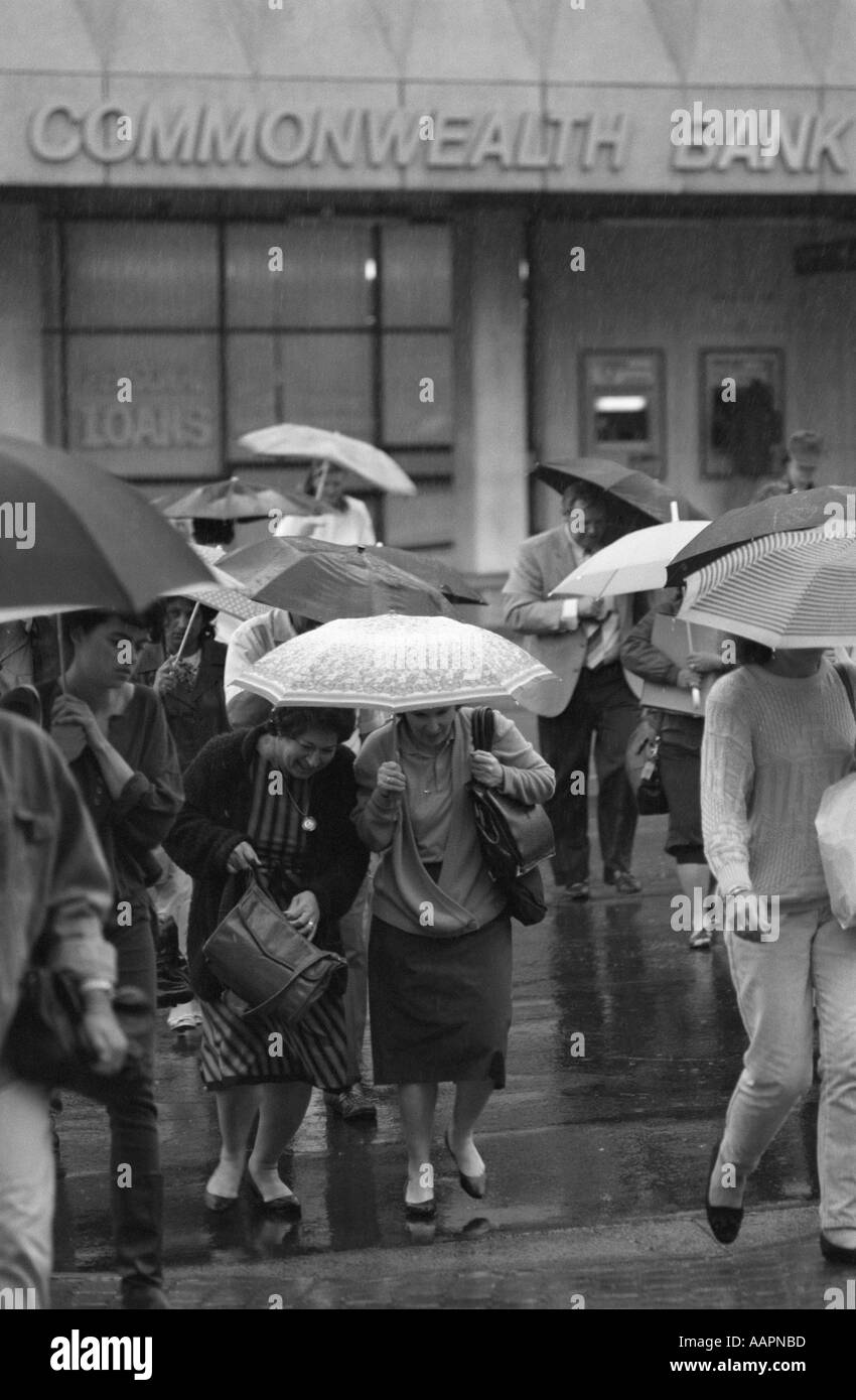 Menschen mit Regenschirmen in Starkregen Kreuzung Straße von der Commonwealth Bank Stadtzentrum von Sydney, Australien. 1987 Stockfoto