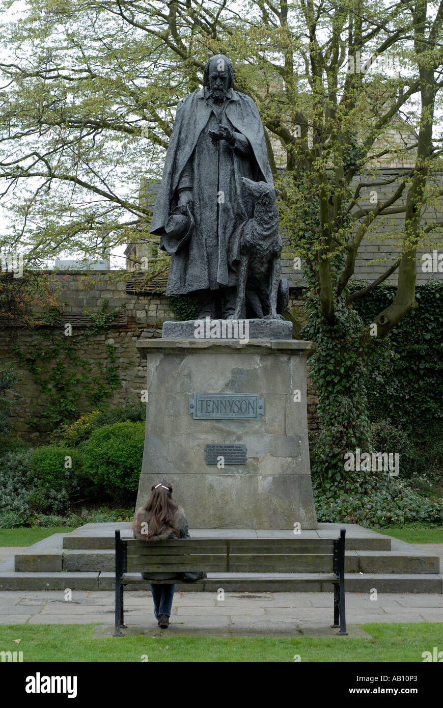 Eine Frau sitzt auf einem Park Bench Comtemplating eine Statue von Alfred Lord Tennyson Tennison in Lincoln Kathedrale Stockfoto