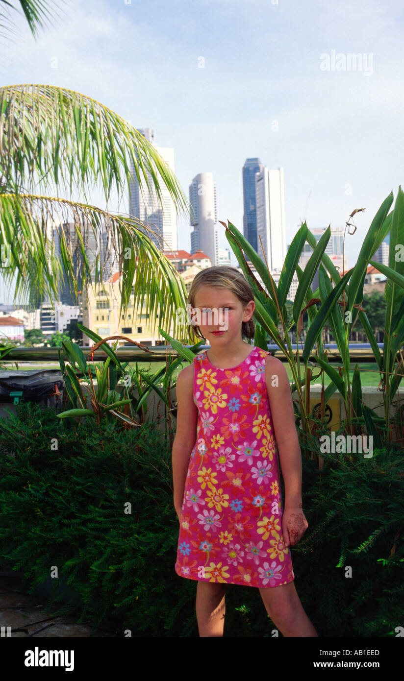 Mädchen im geblümten Kleid gewöhnungsbedürftig ihre erste Reise ins Ausland und die tropische Hitze mit Skyline von Singapur Stockfoto