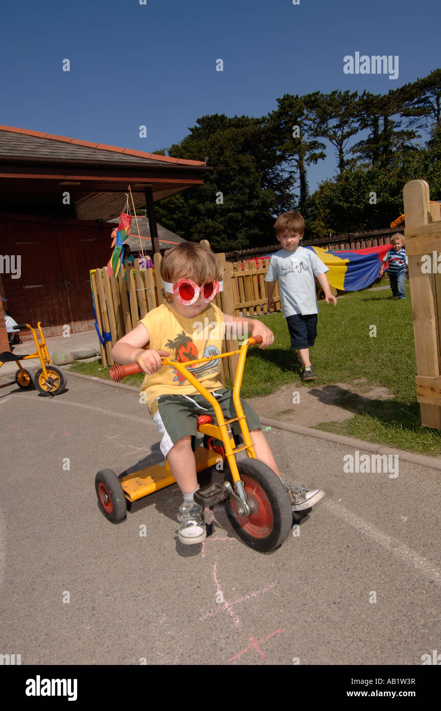 Leiter Gymraeg Aberystwyth walisische Sprache Grundschüler spielen im Freien bei Sonnenschein auf Dreirad Stockfoto