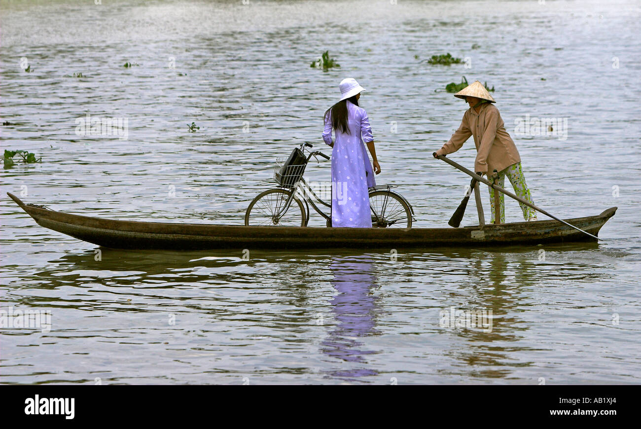 Frau in konische Hut Paddlling Frau in Ao Dai mit Fahrrad in Fähre über den Fluss Mekong Delta Vietnam Stockfoto