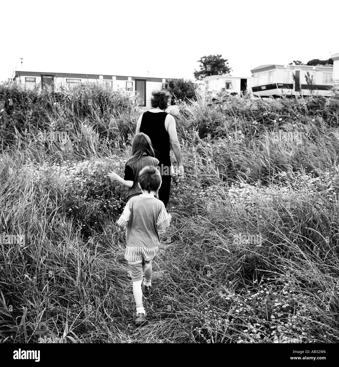 Ein Vater geht durch eine Wiese mit seinen Kindern zu einem Wohnwagen während des Urlaubs in Dorset, Großbritannien. Stockfoto