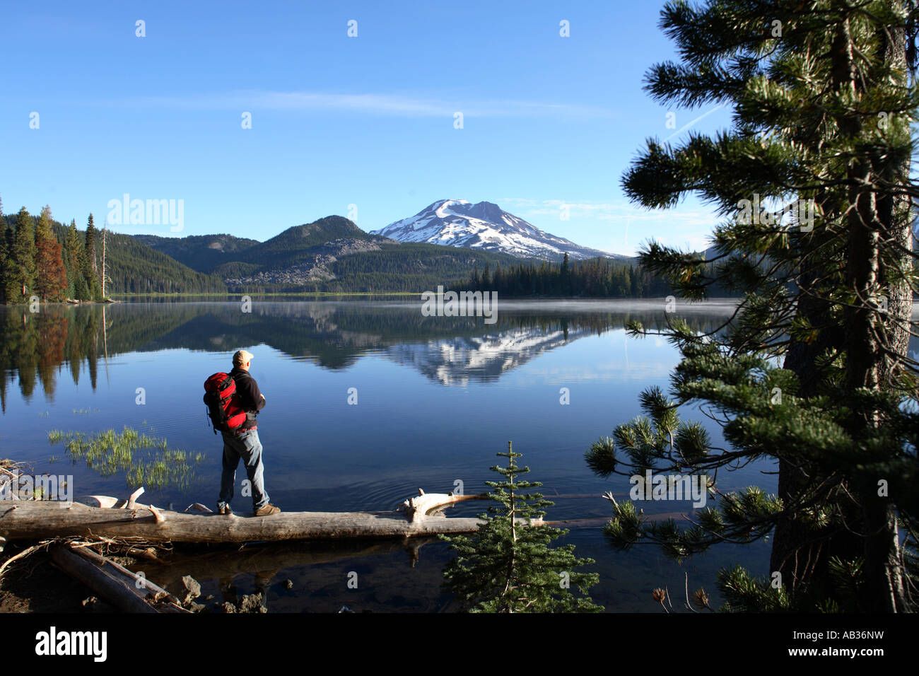Backpacker steht auf Log in Sparks Lake mit South Sister Berg in der Ferne Oregon Stockfoto